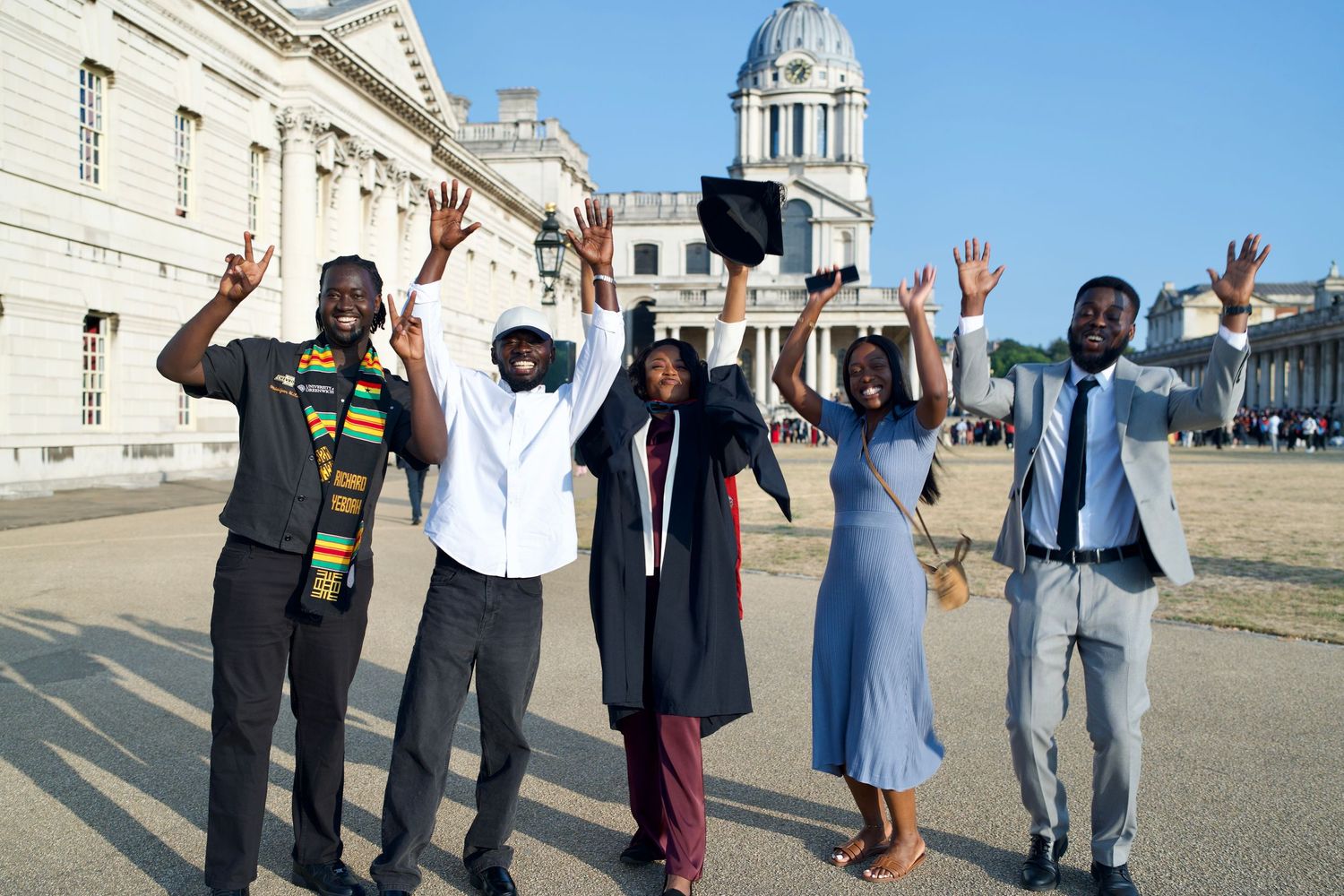 Group of friends celebrating graduation outdoors at Old Royal Naval College in Greenwich by ARIETA Studios.