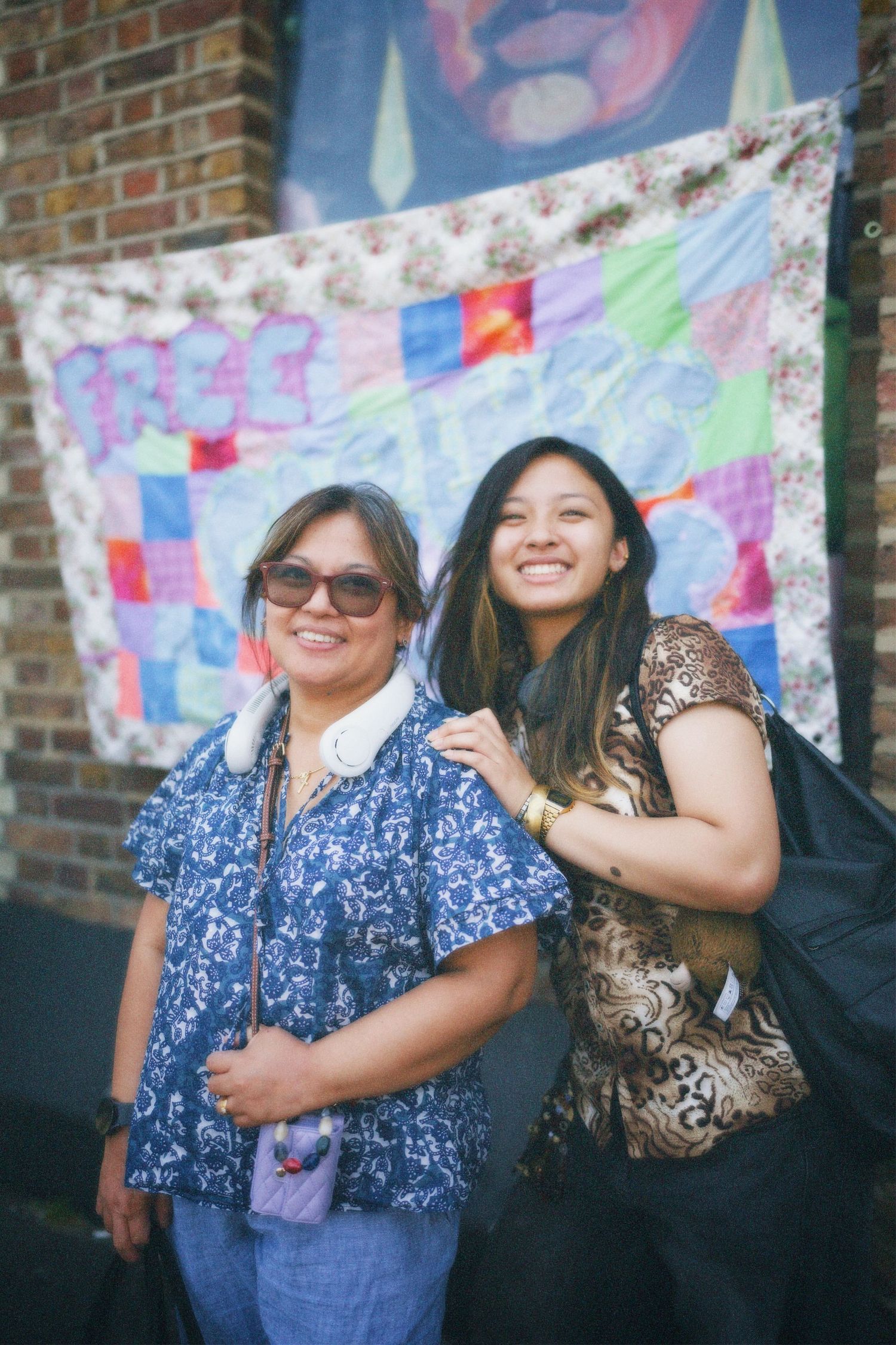 Mother and daughter smiling warmly together in front of a colourful textile backdrop at the Hackney clothes swap.