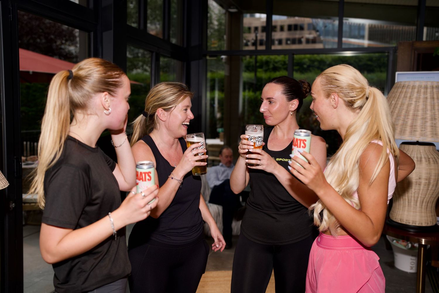 Group of women holding drinks and socializing at a fitness brand activation in London. Commercial lifestyle photography by ARIETA Studios.
