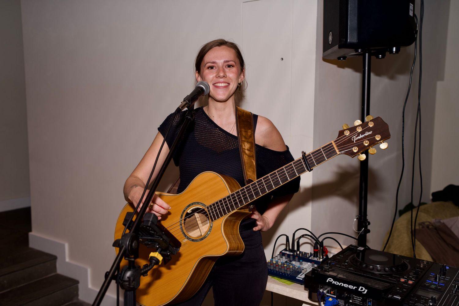 Cydney Brown smiling with an acoustic guitar at a microphone during a live music session performance. Photo by ARIETA Studios.