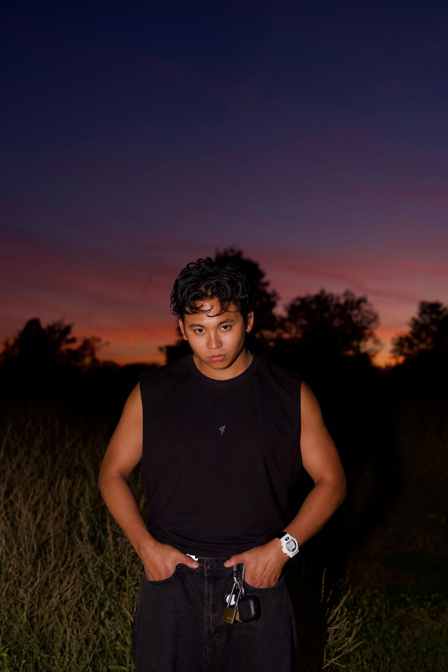 Full-body portrait of a Alastair Arieta nstanding outdoors against a glowing dusk sky.