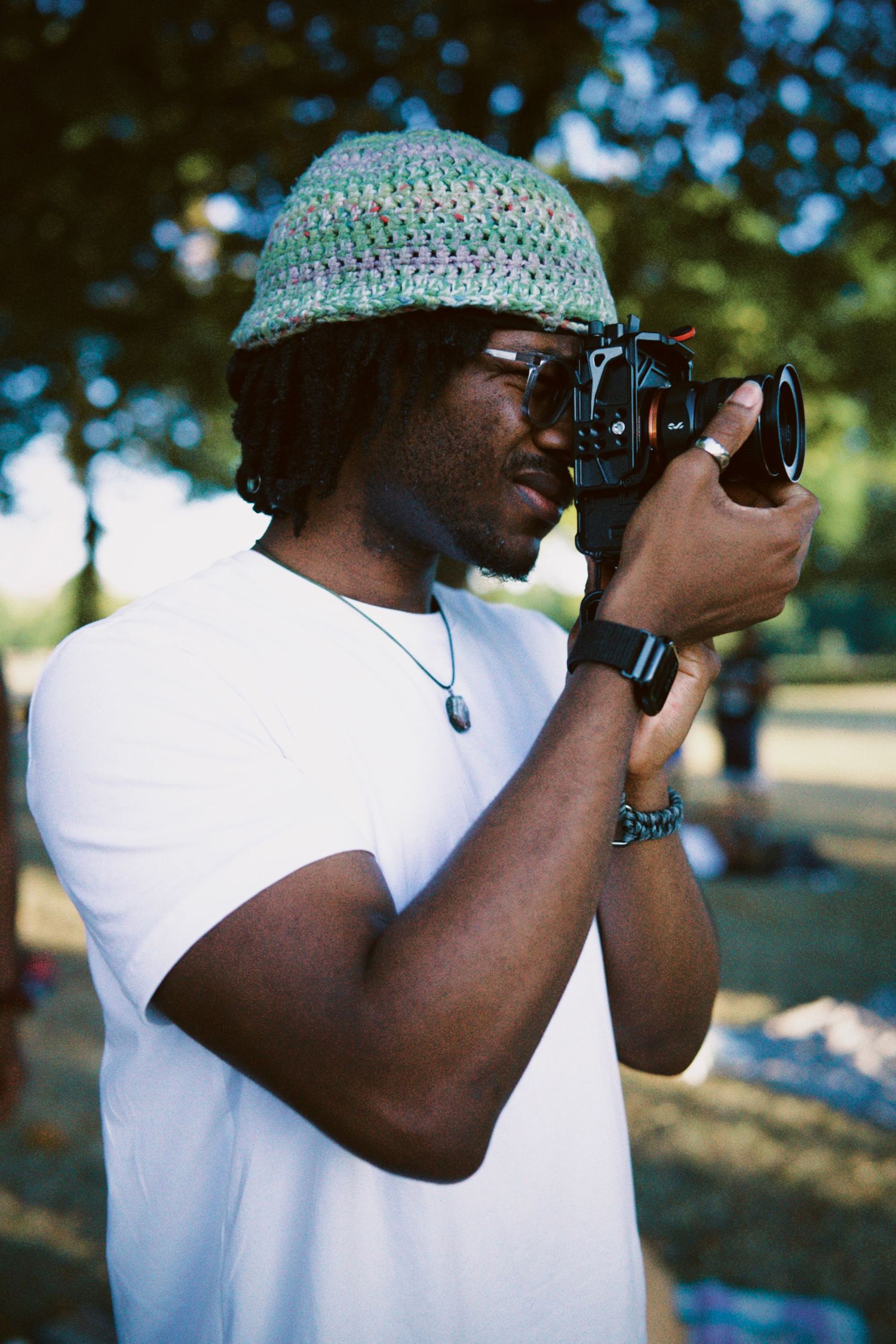 Photographer in knit hat focusing camera lens at summer event by ARIETA Studios.