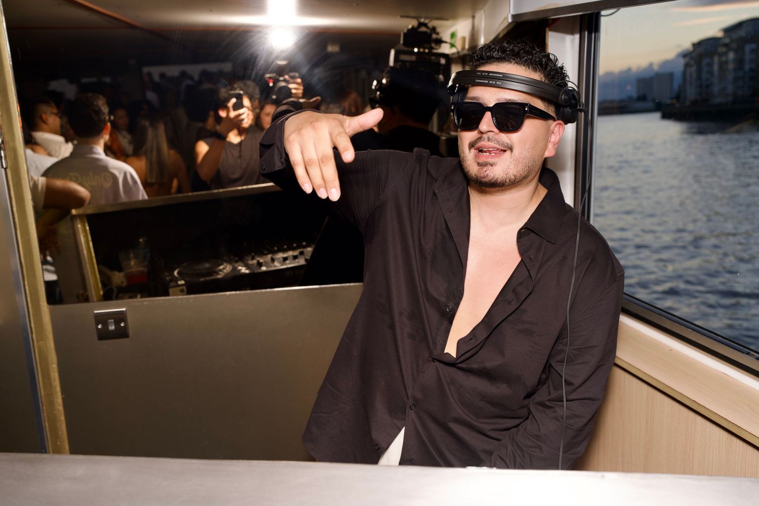 DJ Khriz wearing sunglasses throwing hand signs on boat party deck by ARIETA Studios.