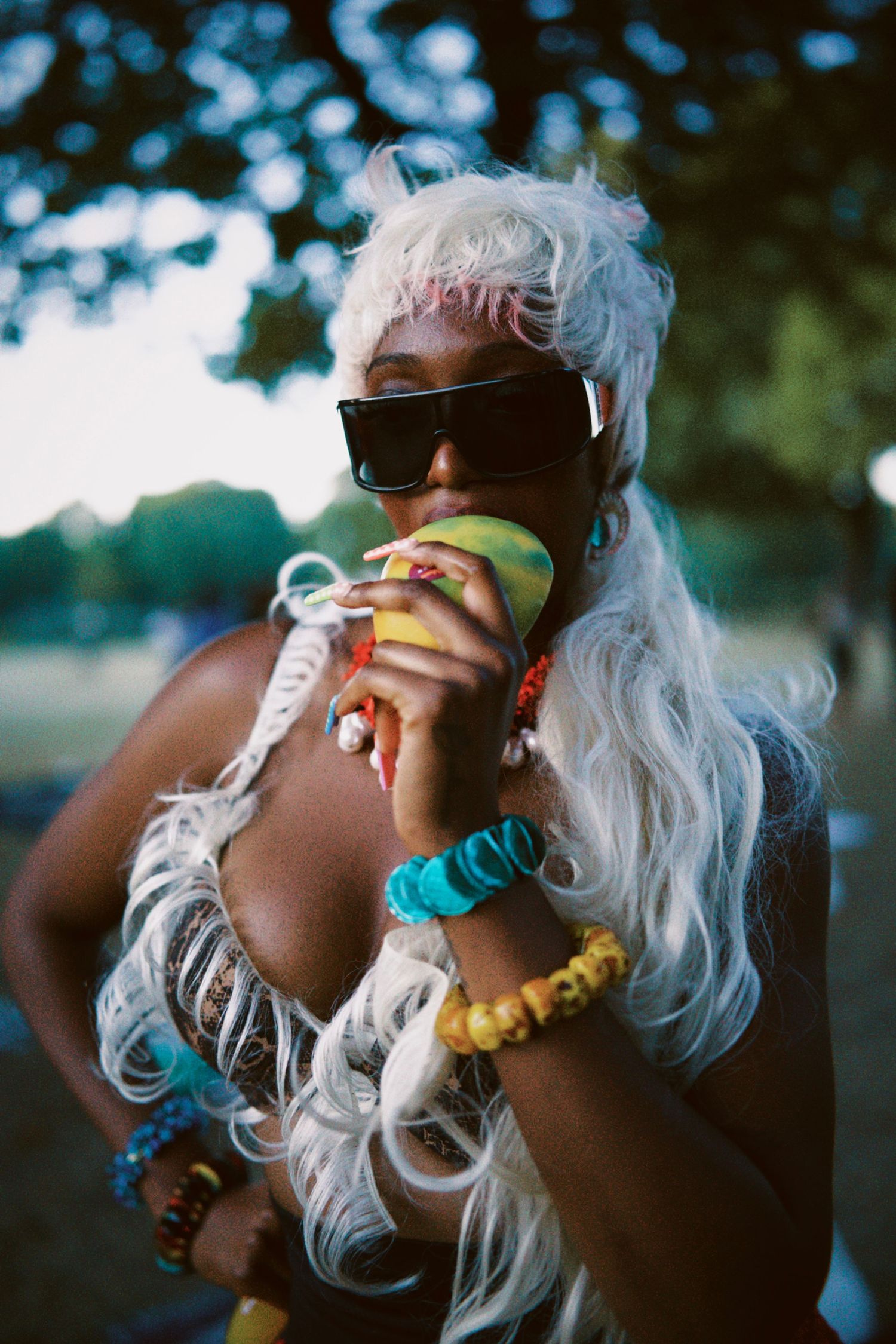 Woman with platinum hair and sunglasses holding green mango by ARIETA Studios.