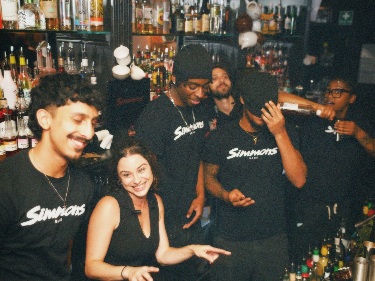 Energetic Simmons bar crew laughing and posing together during a busy night shift. Event photography by ARIETA Studios.