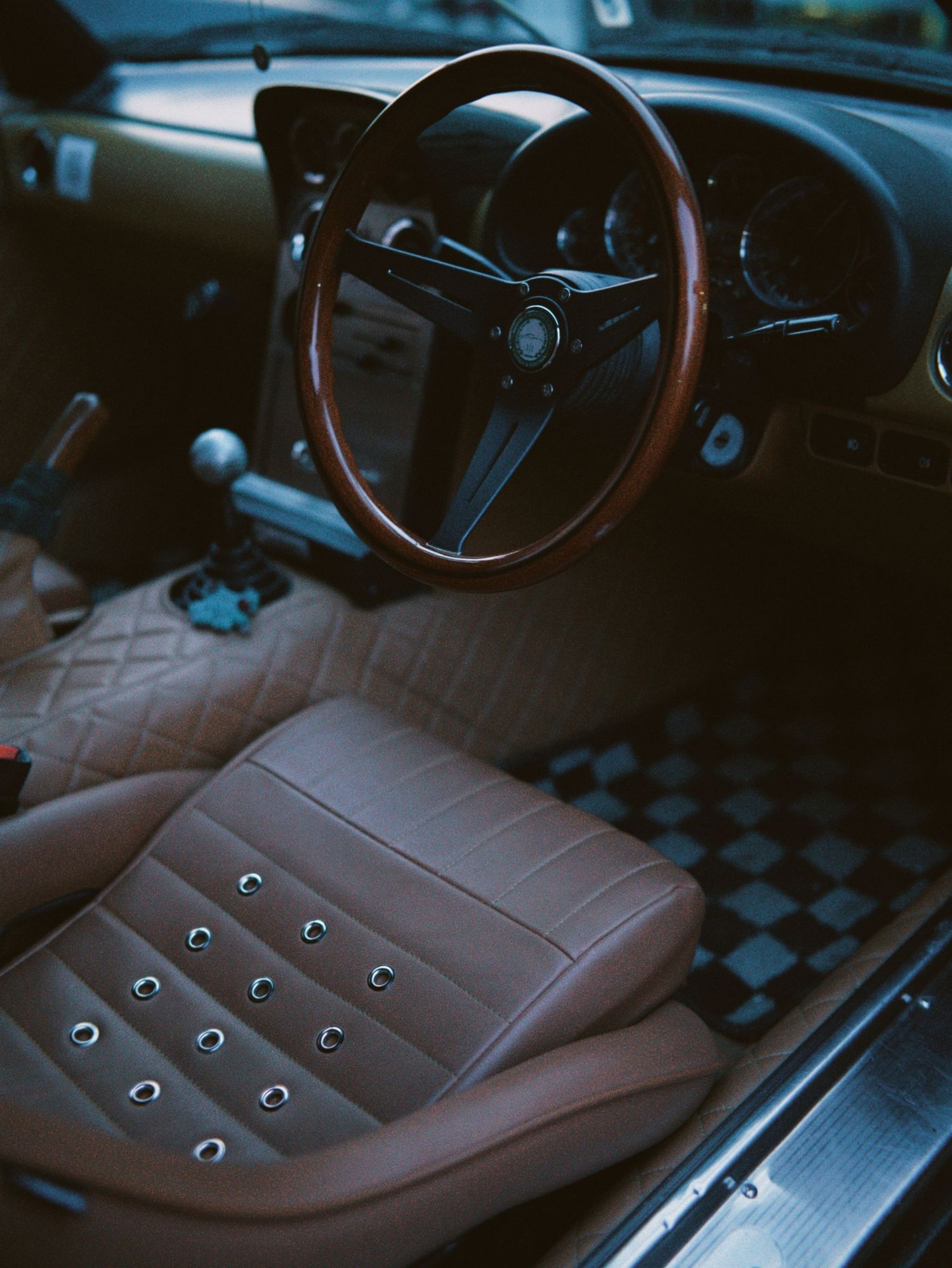 Interior view of a classic car featuring a wooden steering wheel and tan leather seats.