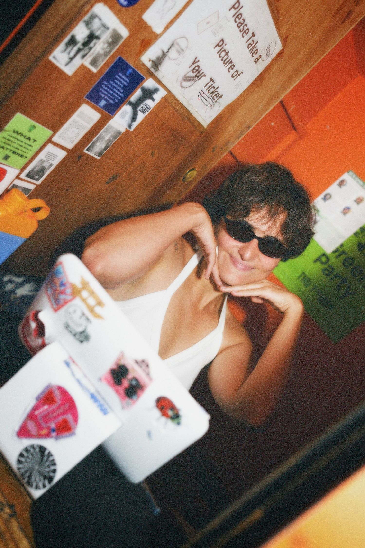 Woman in sunglasses striking a playful pose by the sticker-covered counter at Fashion For Future exchange