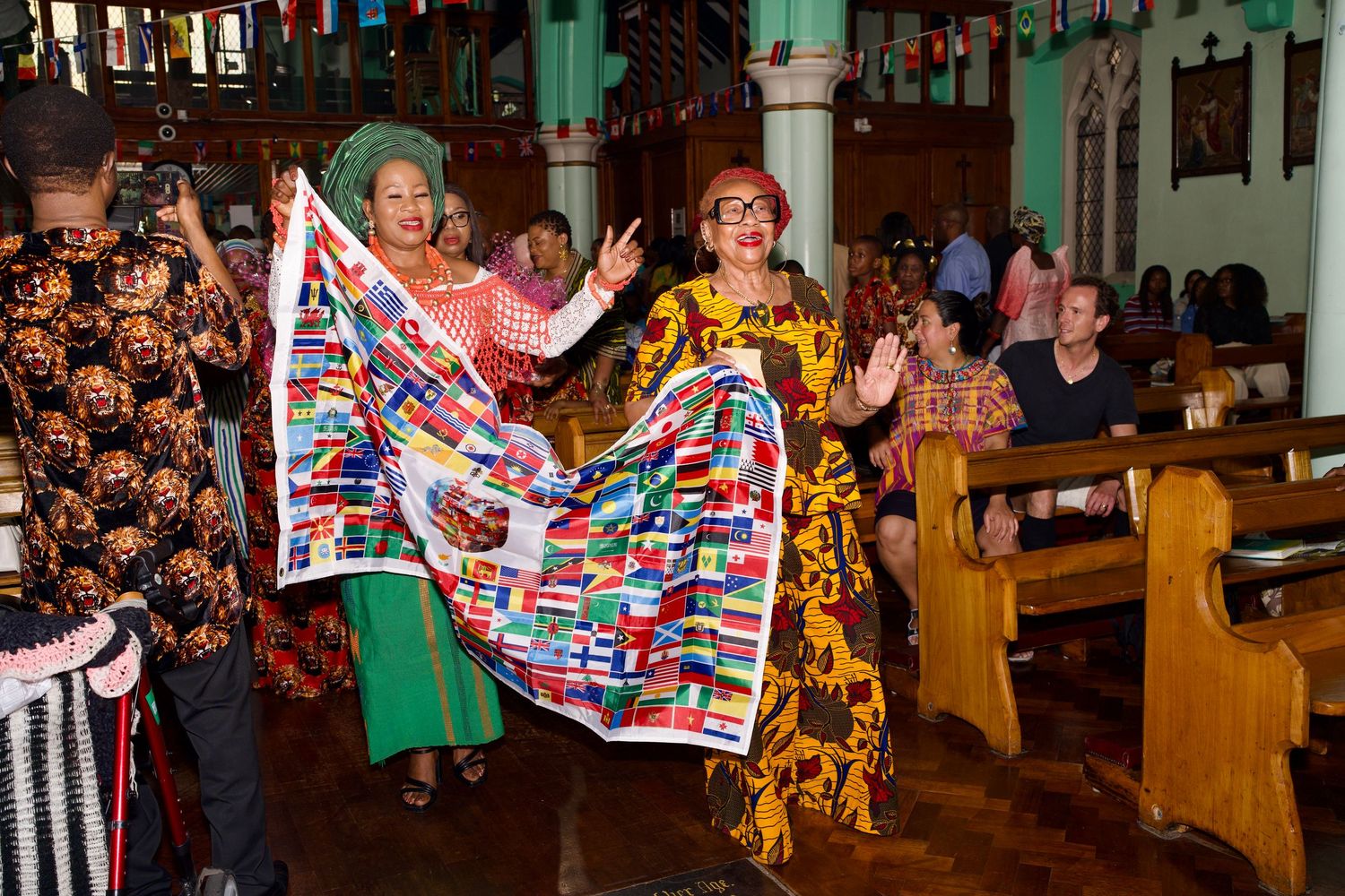 Women in traditional African attire holding a flag banner at a Vibrant Roots cultural event by ARIETA Studios.