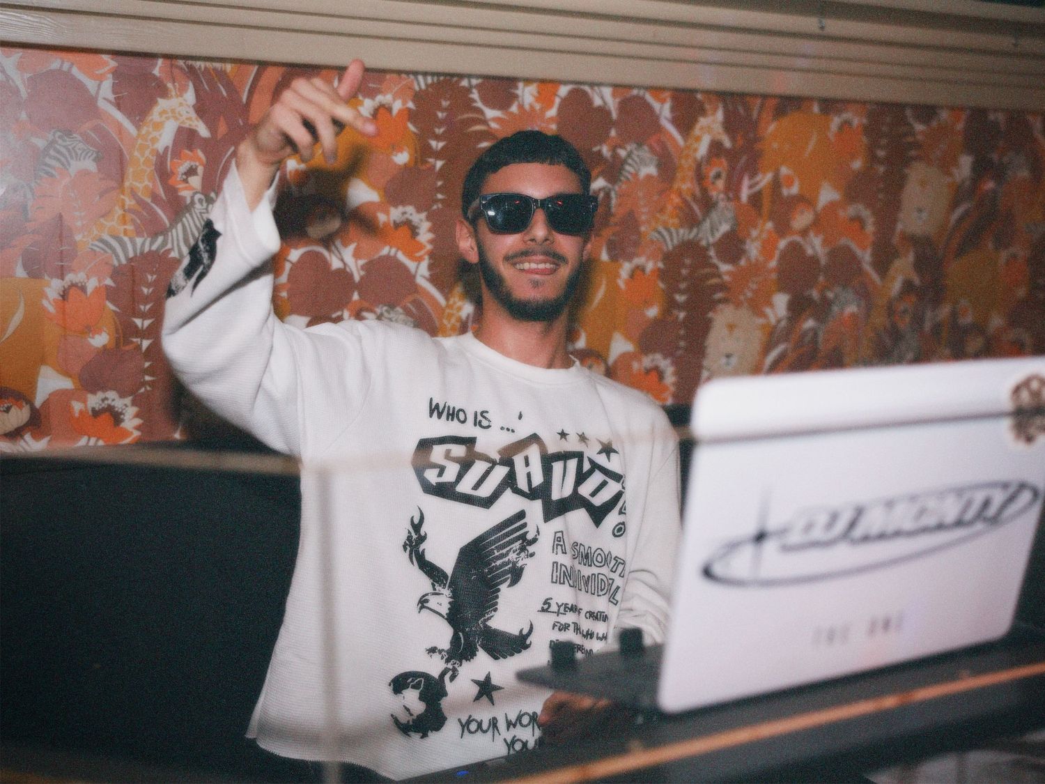 DJ wearing sunglasses mixing music at a laptop controller during a high-energy bar event. Captured by ARIETA Studios.