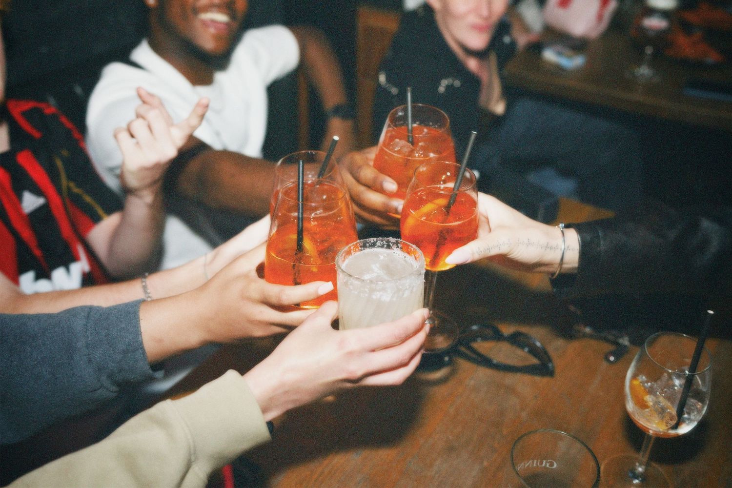 A group of friends gathering and raising glasses of Aperol Spritz cocktails in a collaborative toast by ARIETA Studios.