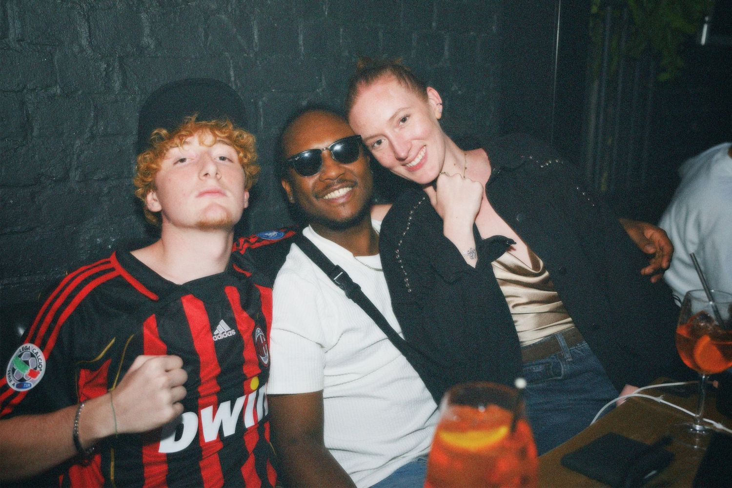 Group of three friends posing closely together and smiling at an indoor bar event captured by ARIETA Studios.