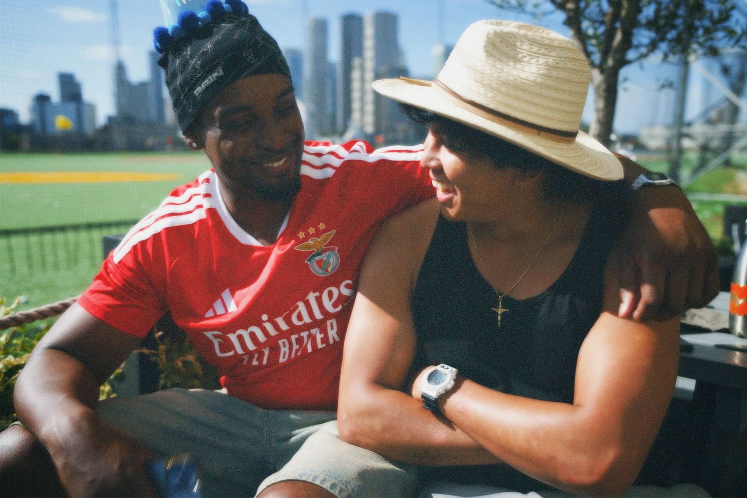 Candid outdoor portrait of two friends, Alastair and Kevin laughing together in summer hats during golden hour.
