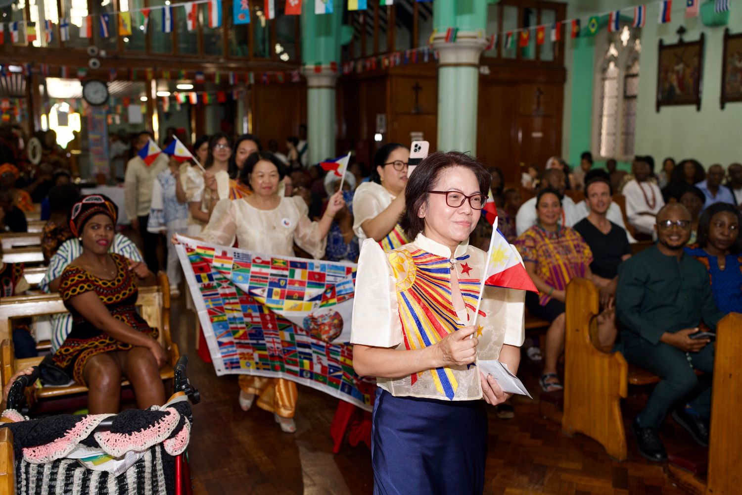 Woman holding small Philippines flag during church Culture Day procession by ARIETA Studios.