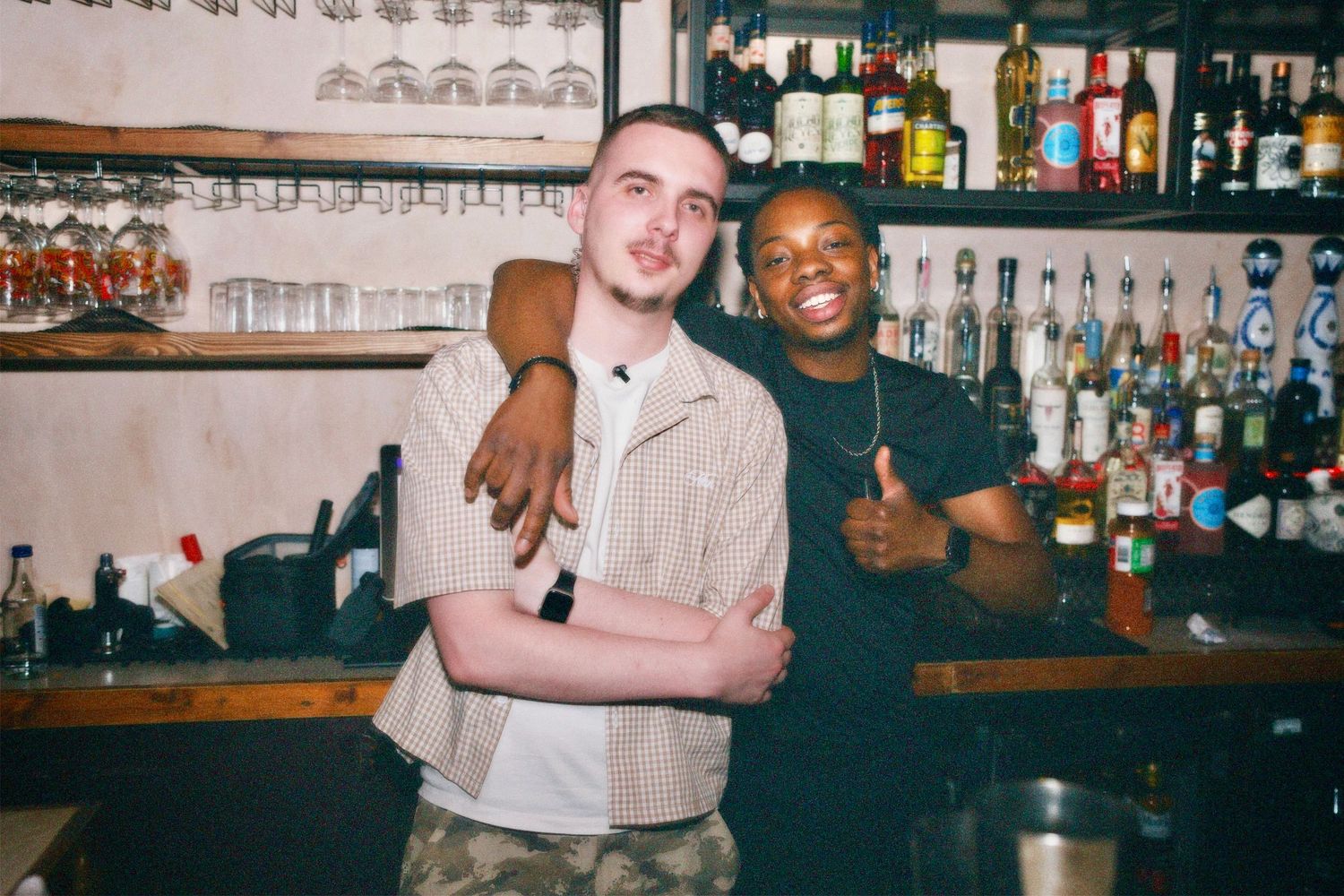Two men posing together behind bar counter at London venue event by ARIETA Studios. (