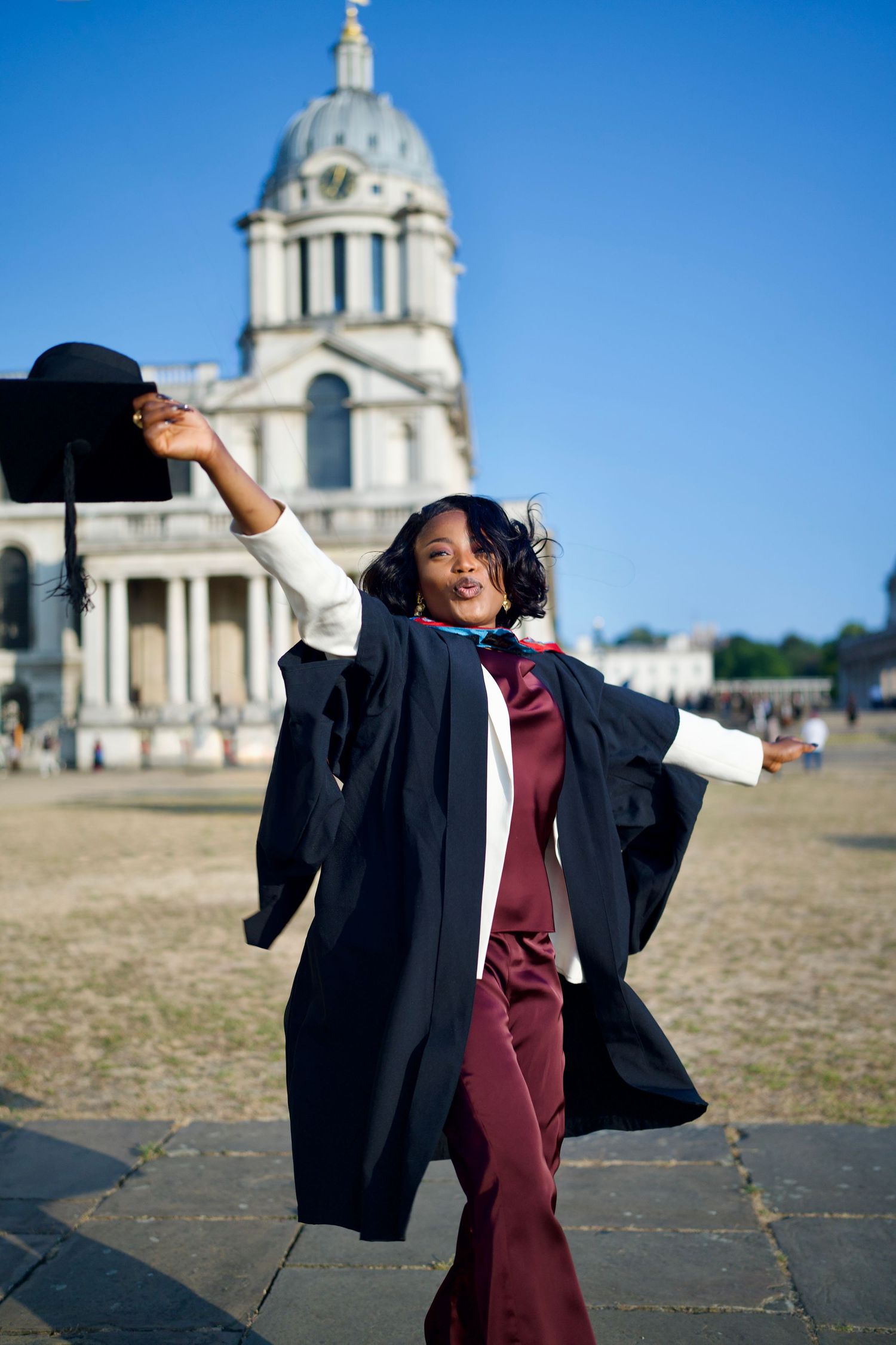 Graduate posing joyfully in gown outdoors at Old Royal Naval College Greenwich by ARIETA Studios.