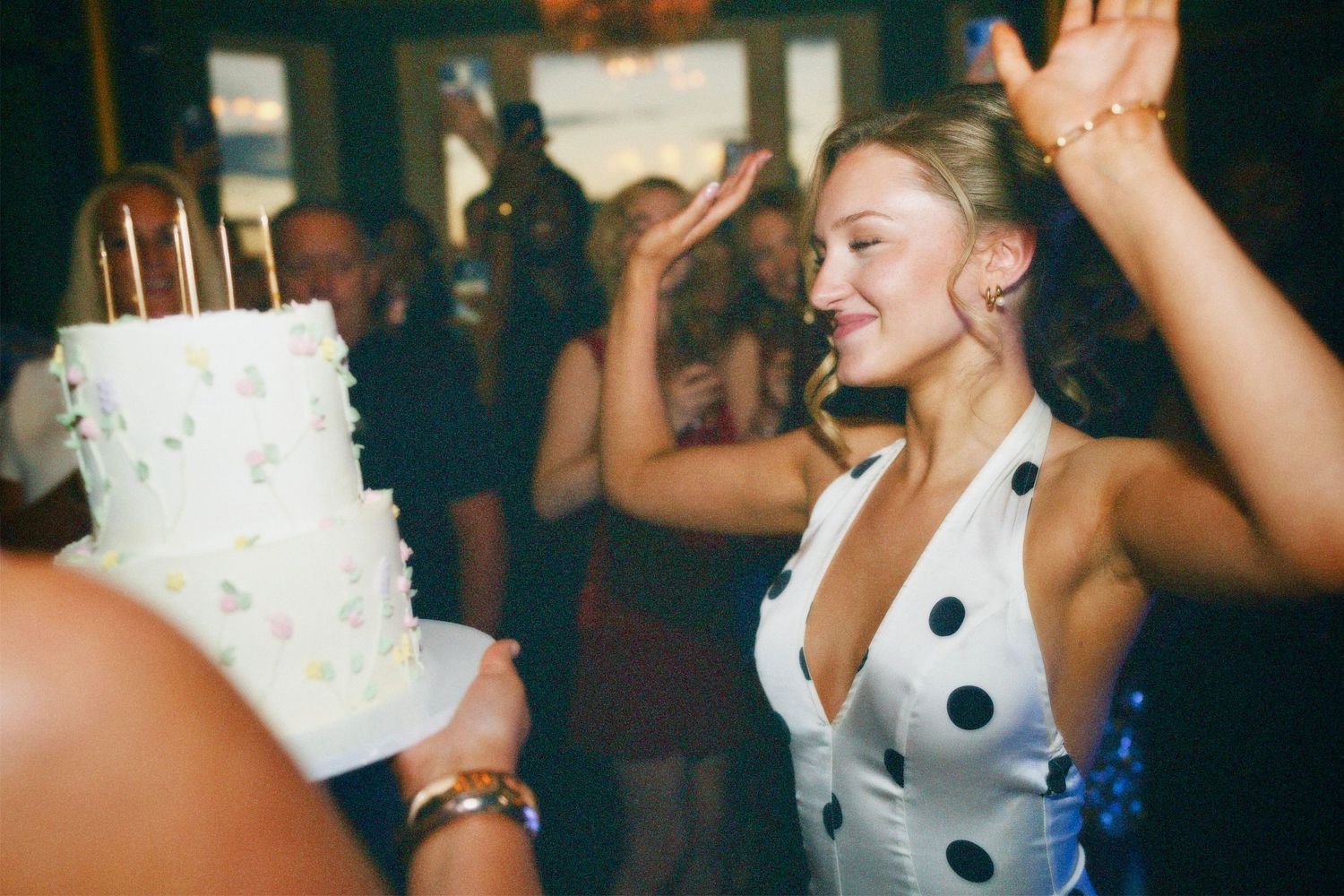 Birthday celebrant Amelia Hurst in polka dot dress dancing near two-tier birthday cake at party covered by ARIETA Studios.