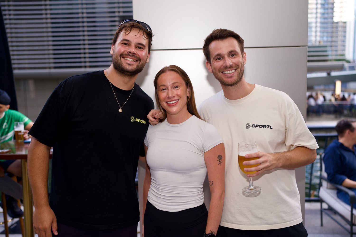 Three friends smiling and posing together with drinks on an outdoor terrace.
