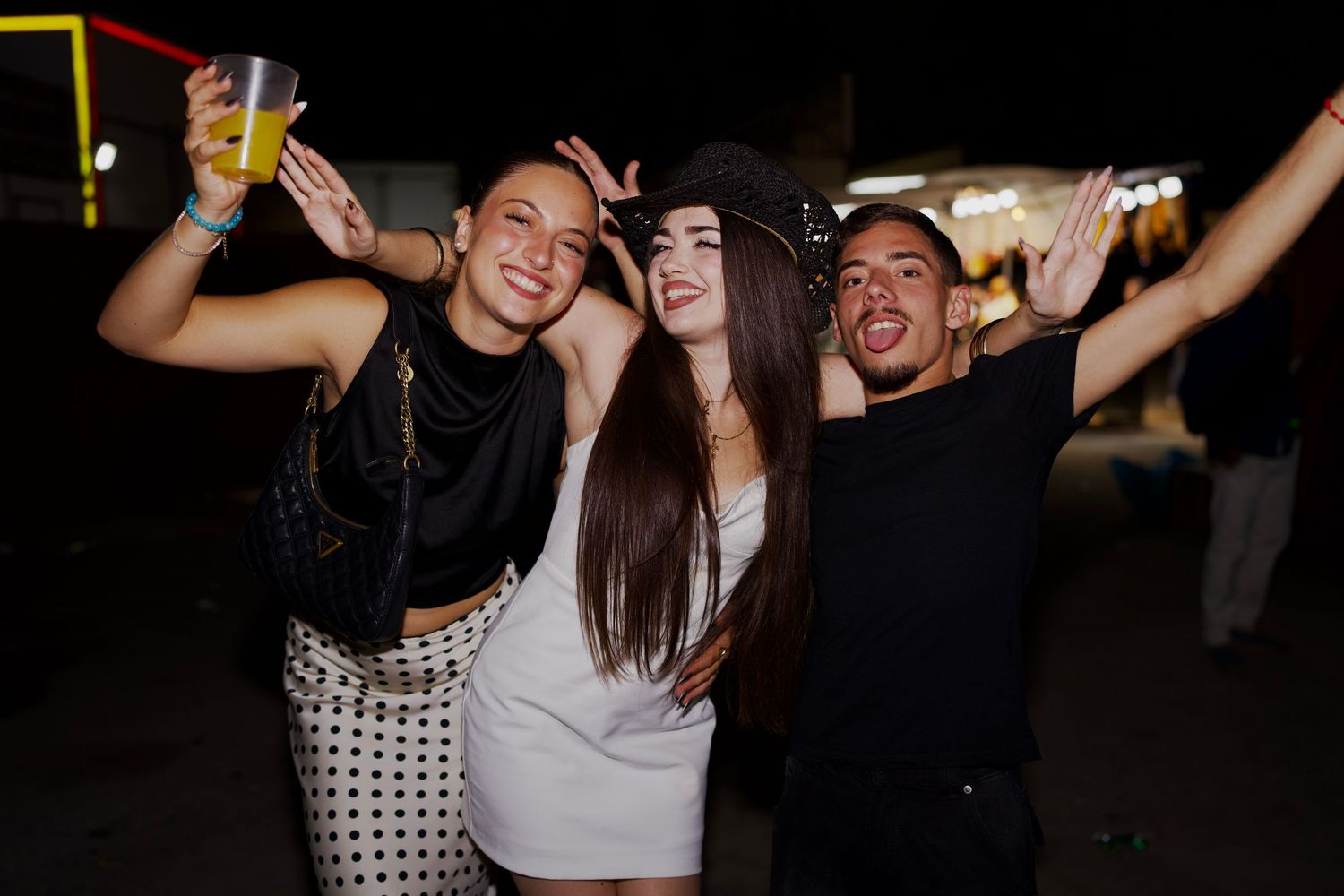 Three friends posing and smiling with drinks at Feria de Málaga / Tres amigos posando y sonriendo con copas en la Feria de Málaga