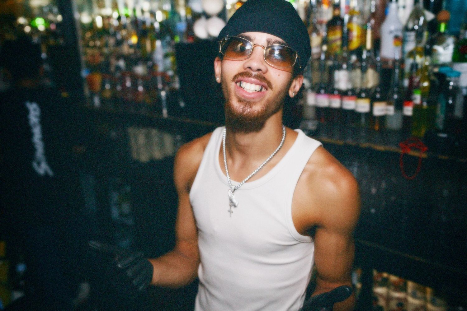 Bartender smiling behind bar counter at London nightlife event by ARIETA Studios.