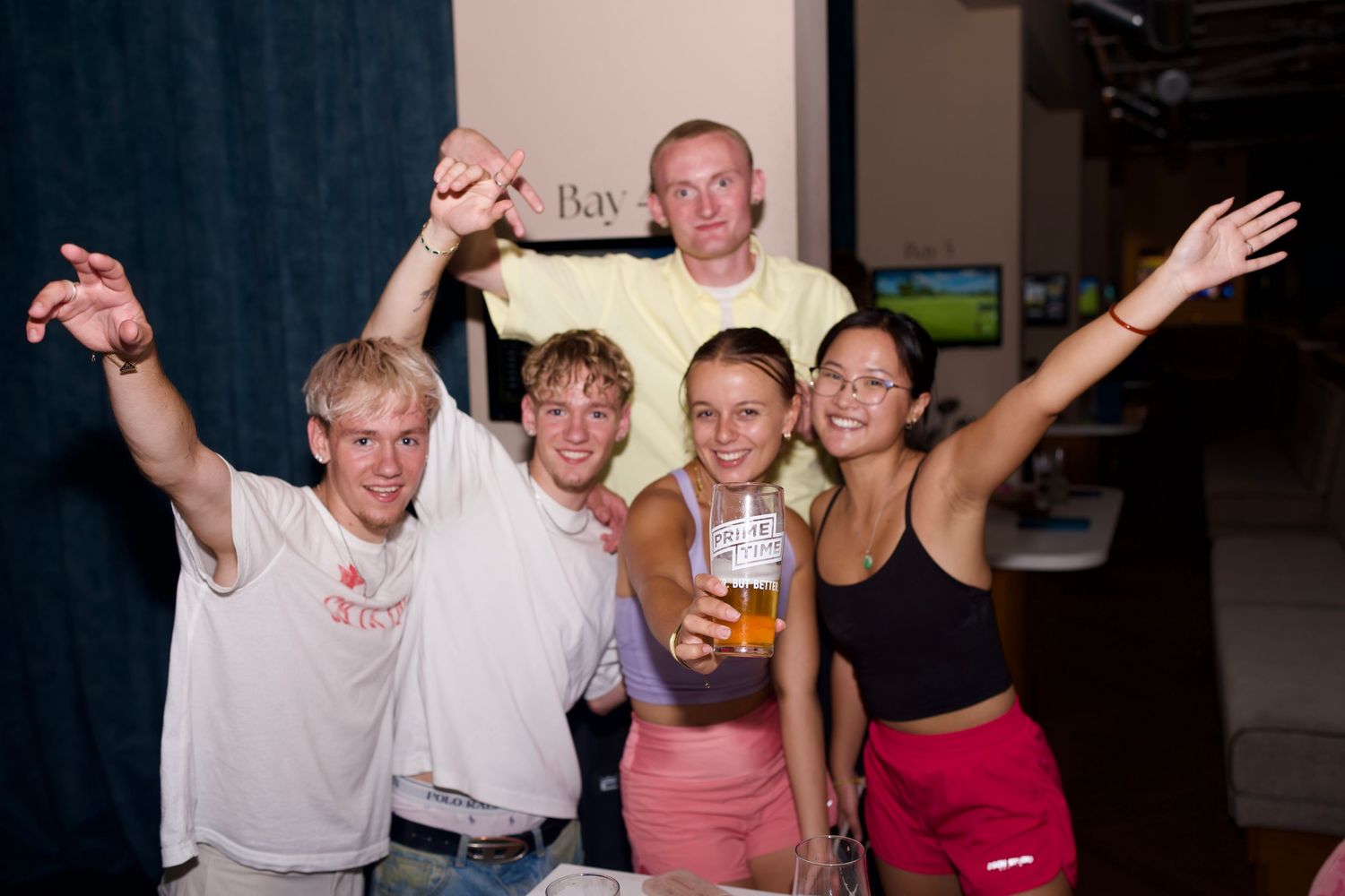 Excited group of friends cheering, raising drinks, and celebrating indoors.