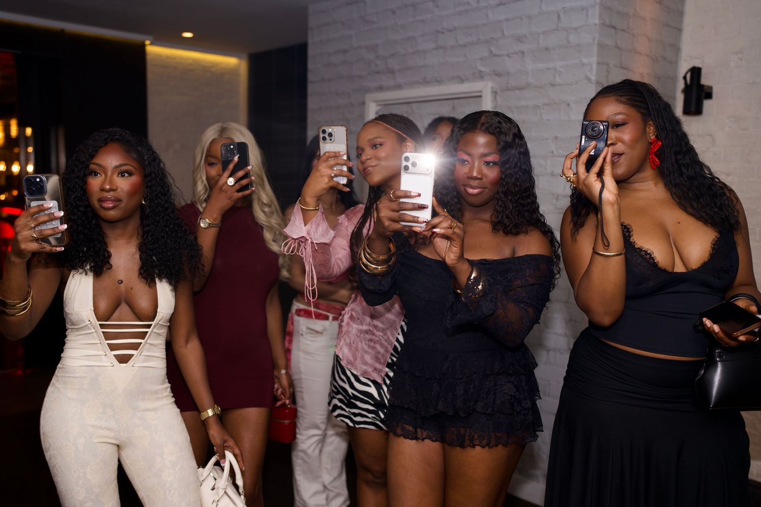 A group of fashionable women taking phone photos during a luxury girls' night out editorial by ARIETA STUDIOS.
