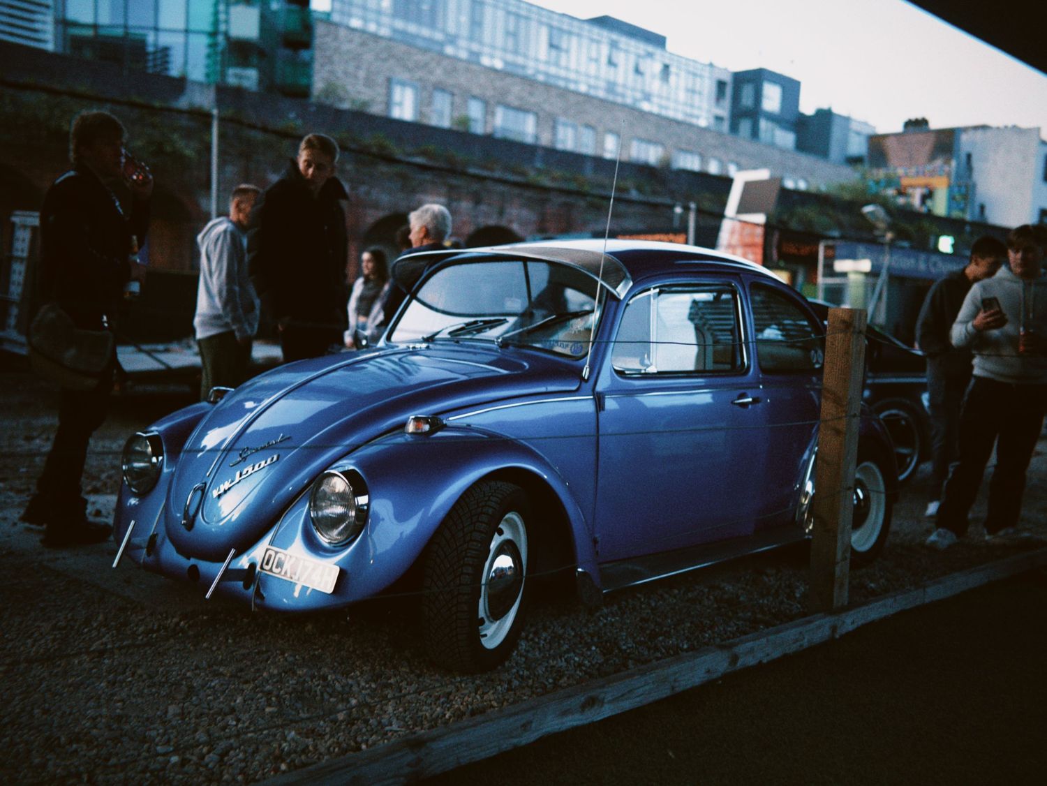 A classic blue Volkswagen Beetle parked outside a venue at dusk.