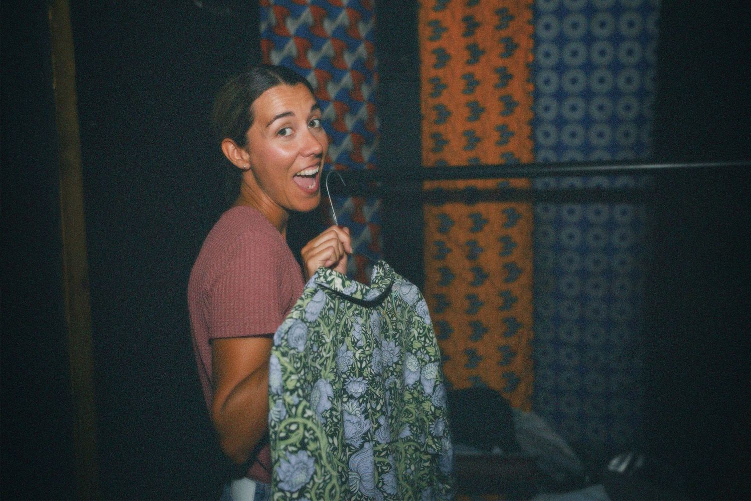 Woman holding up a patterned vintage top while smiling near clothing racks at Hackney clothes swap