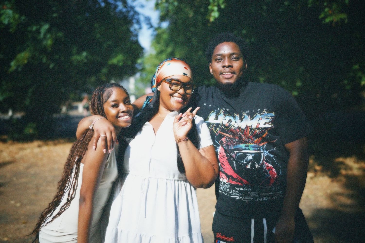 Group portrait of three friends posing together outdoors under park trees.