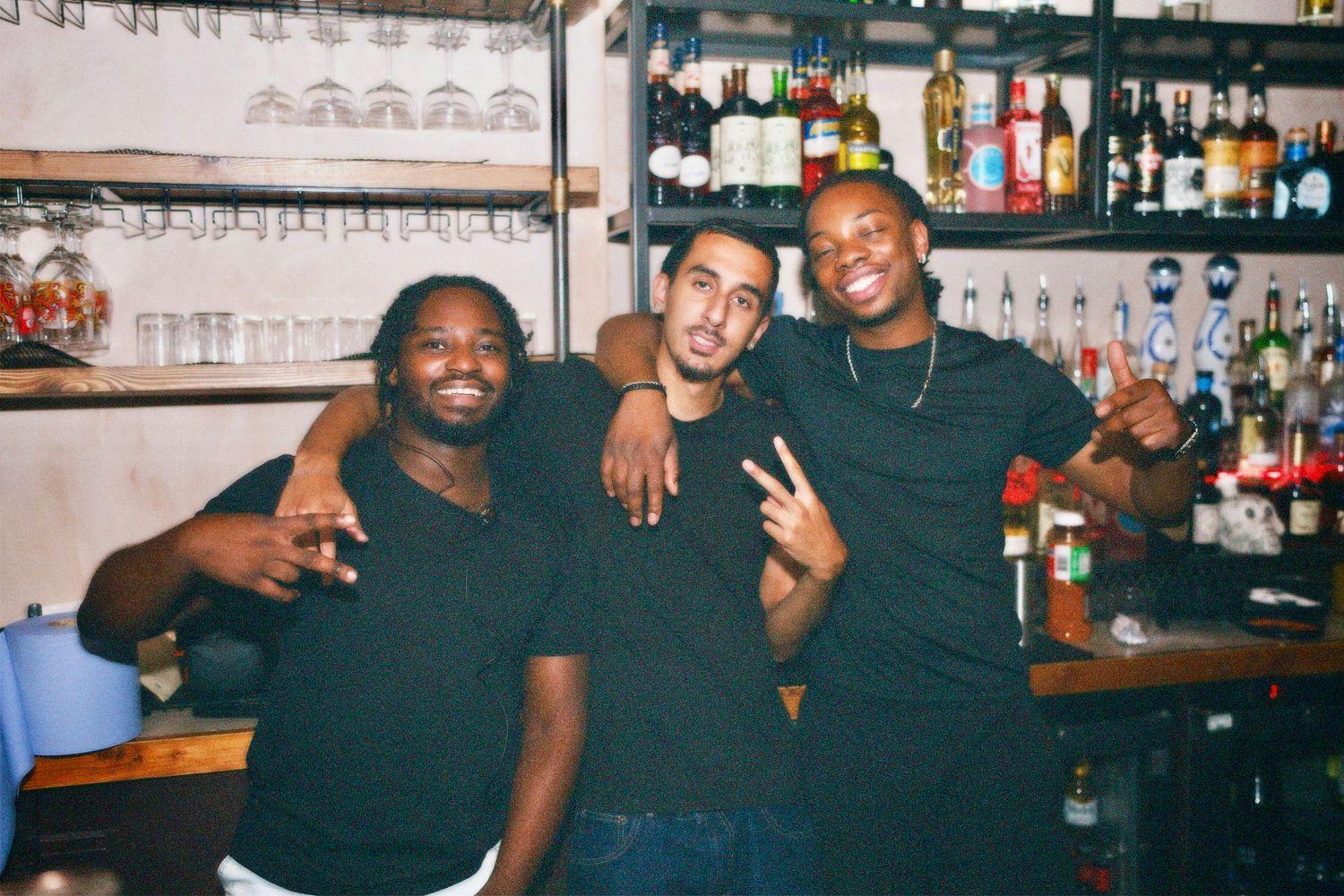 Three men posing together behind bar counter at London party event by ARIETA Studios.