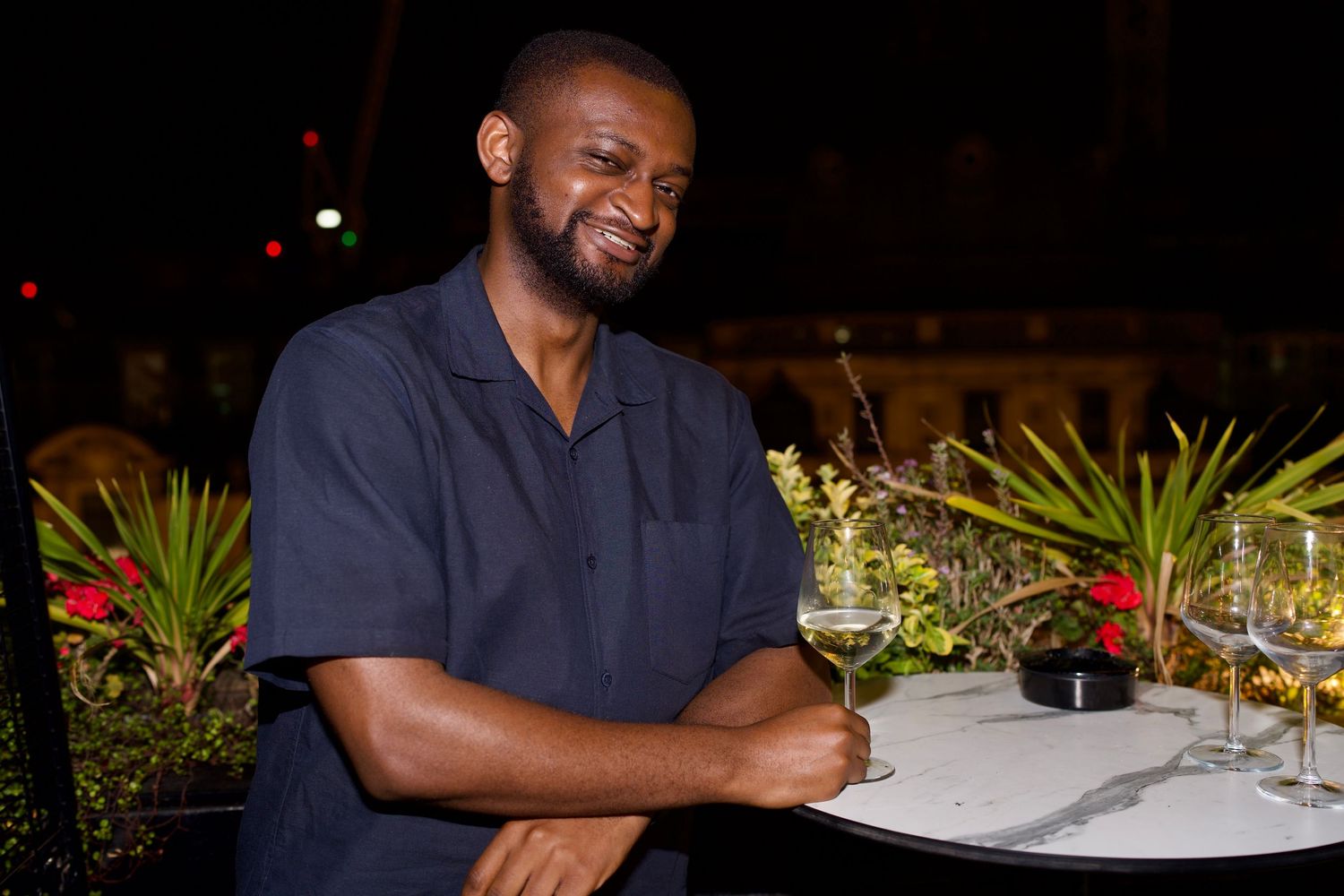 A man holding a drink at a marble table during a luxury rooftop nightlife editorial by ARIETA STUDIOS.