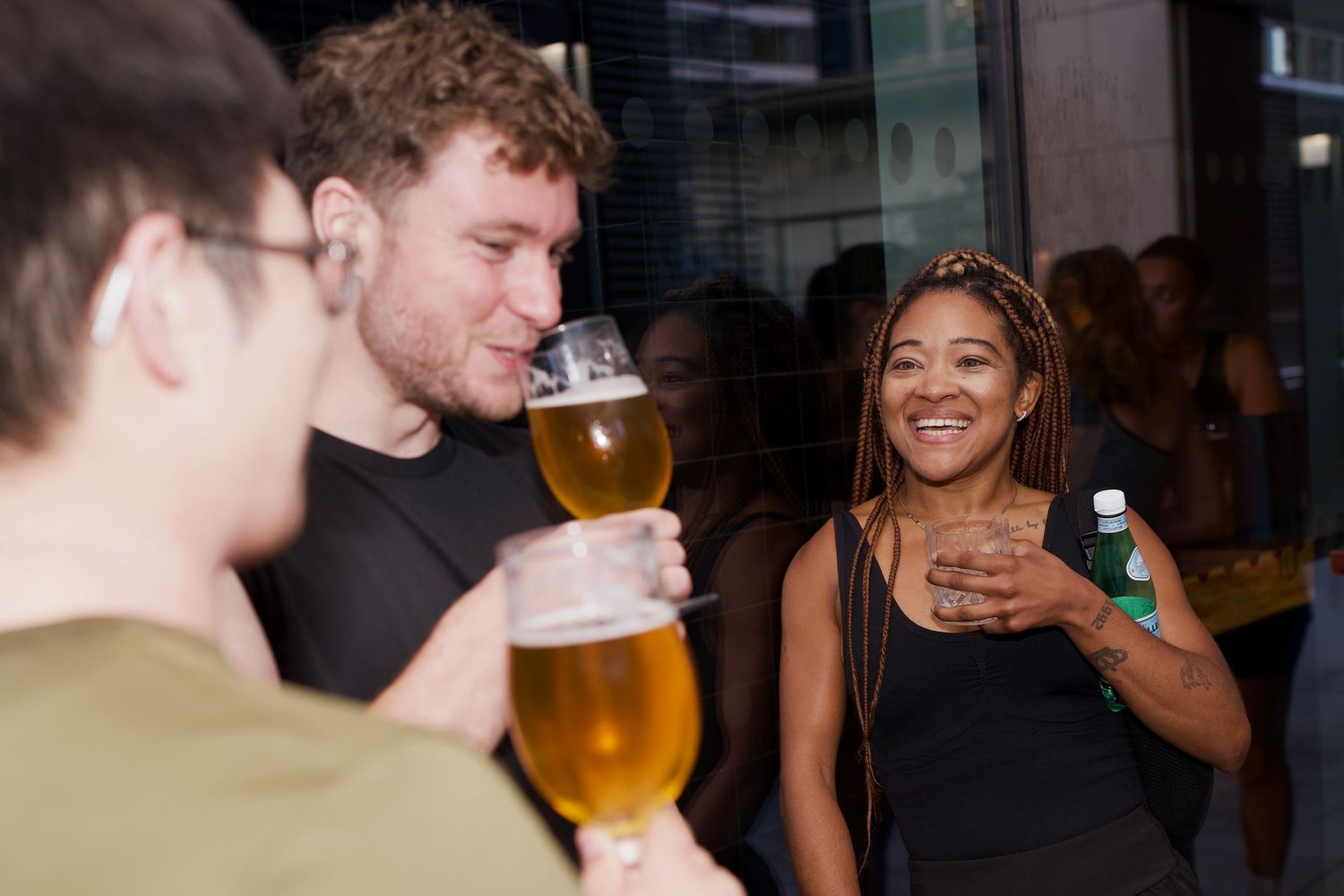 Friends laughing and raising glasses of beer together at a London run event by ARIETA Studios.