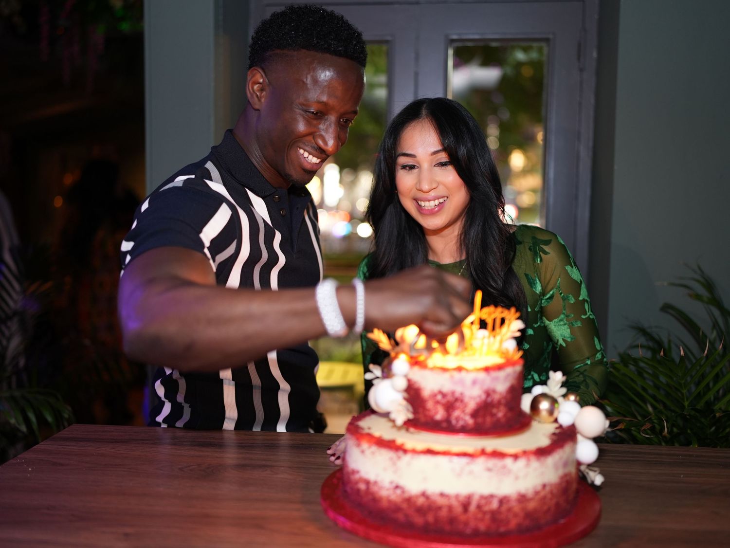 Couple smiling together behind birthday cake with lit candles by ARIETA Studios.