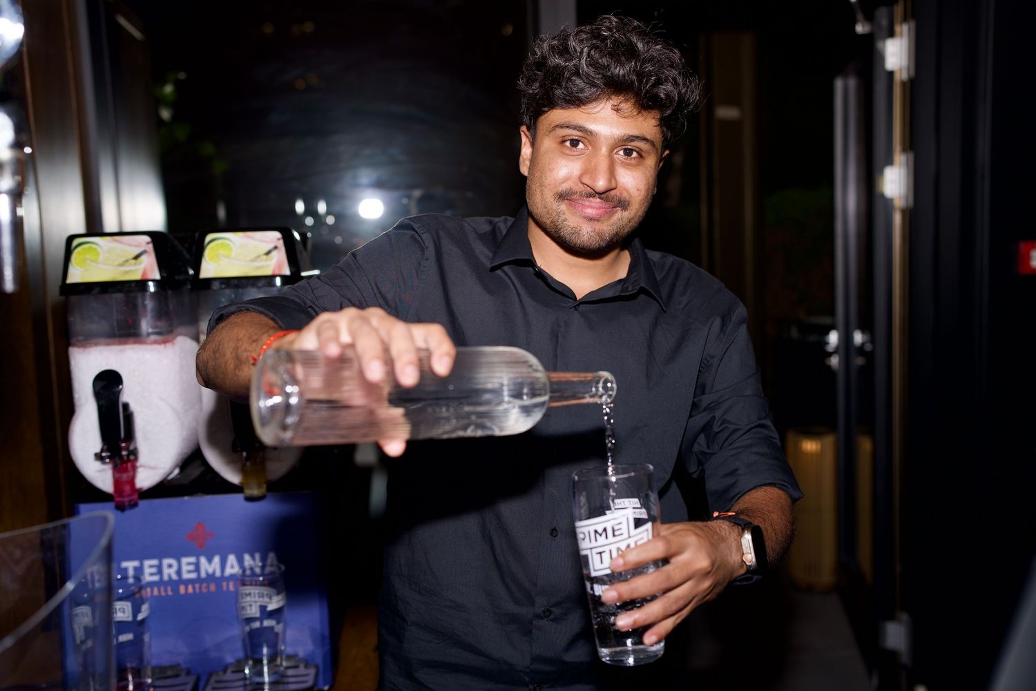 A smiling bartender pouring a drink for guests during a busy commercial evening event. Photo by ARIETA Studios.