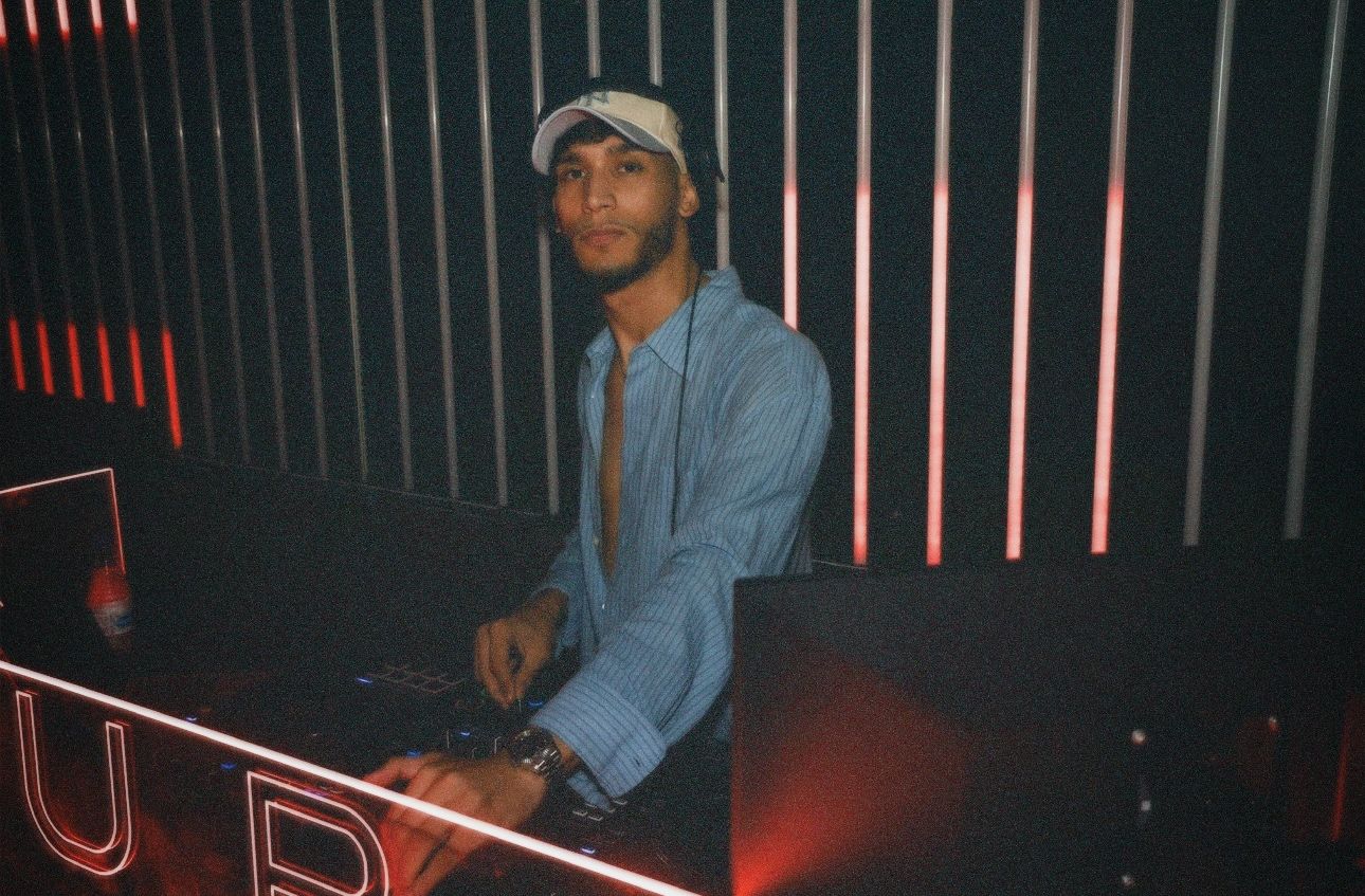 DJ posing behind the decks. / DJ posando tras la cabina bajo luces de neón.