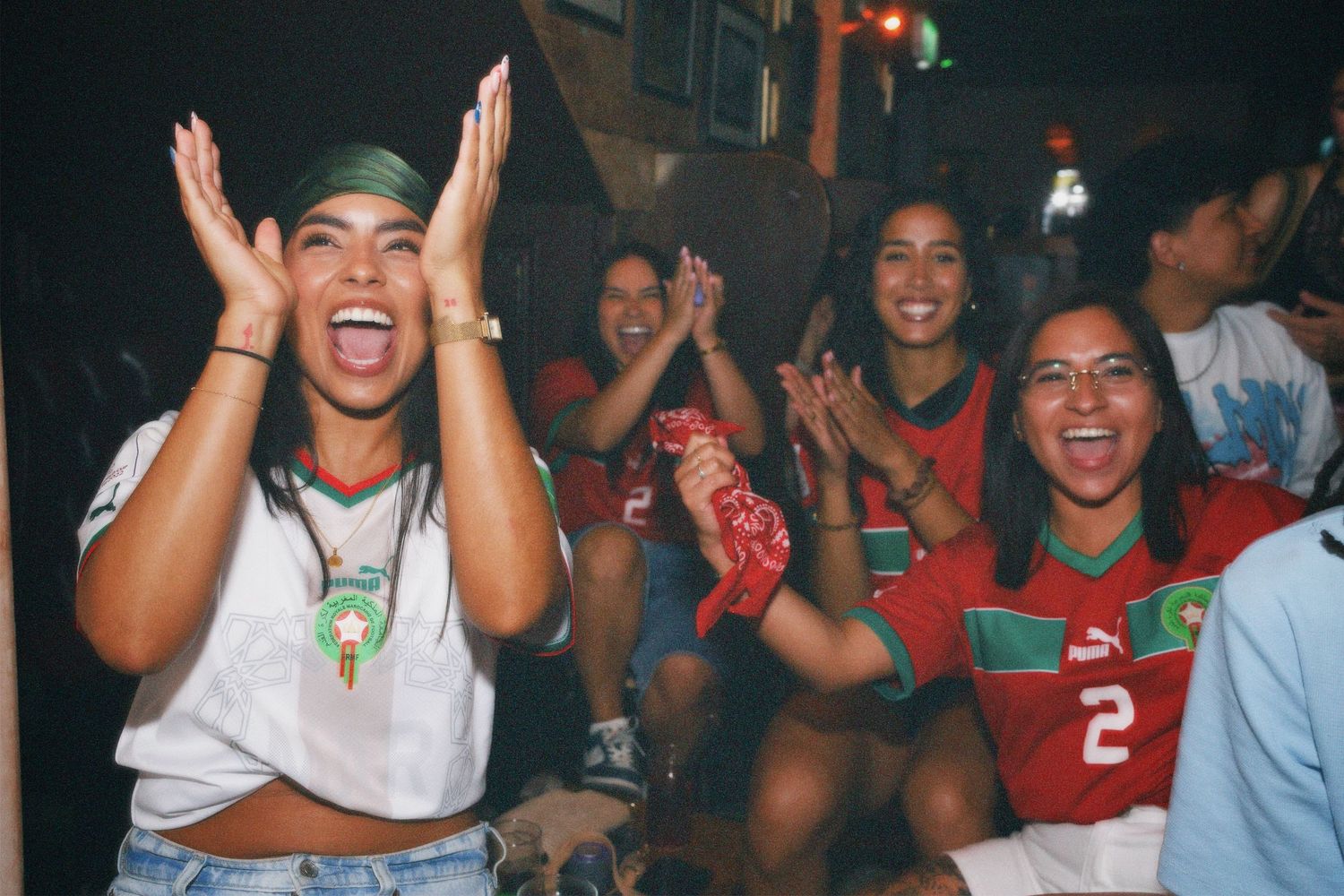 Women cheering in Morocco football jerseys at La Tribu event by ARIETA Studios.