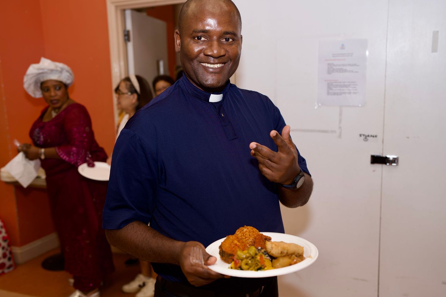 Priest smiling and holding a plate of traditional food at Culture Day by ARIETA Studios.