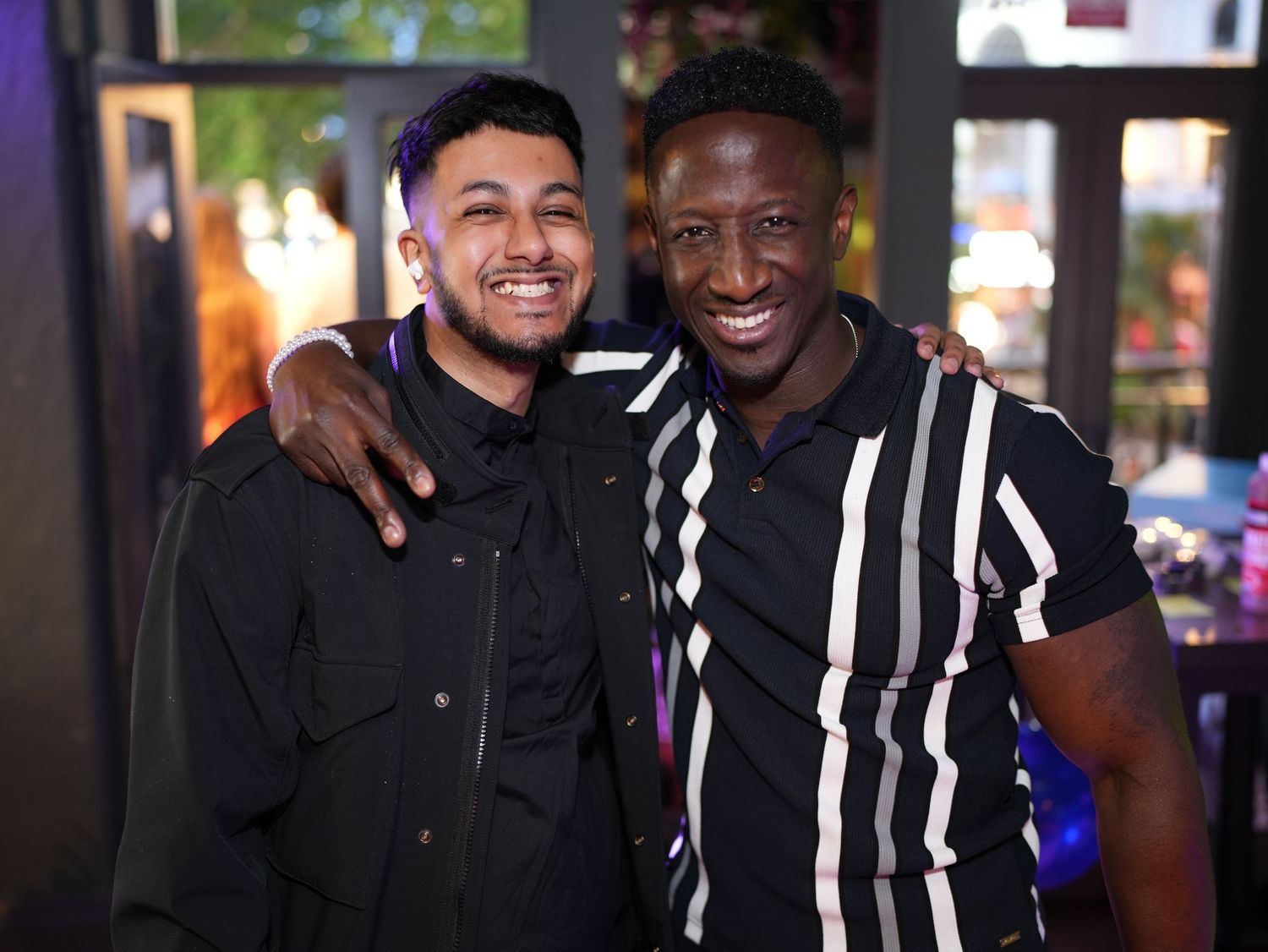 Two men smiling with their arms around each other's shoulders at a night event.