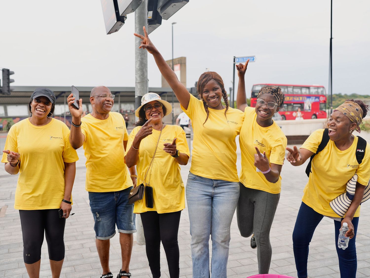 Streams of Joy Erith volunteers in yellow t-shirts cheering together during outreach by ARIETA Studios.