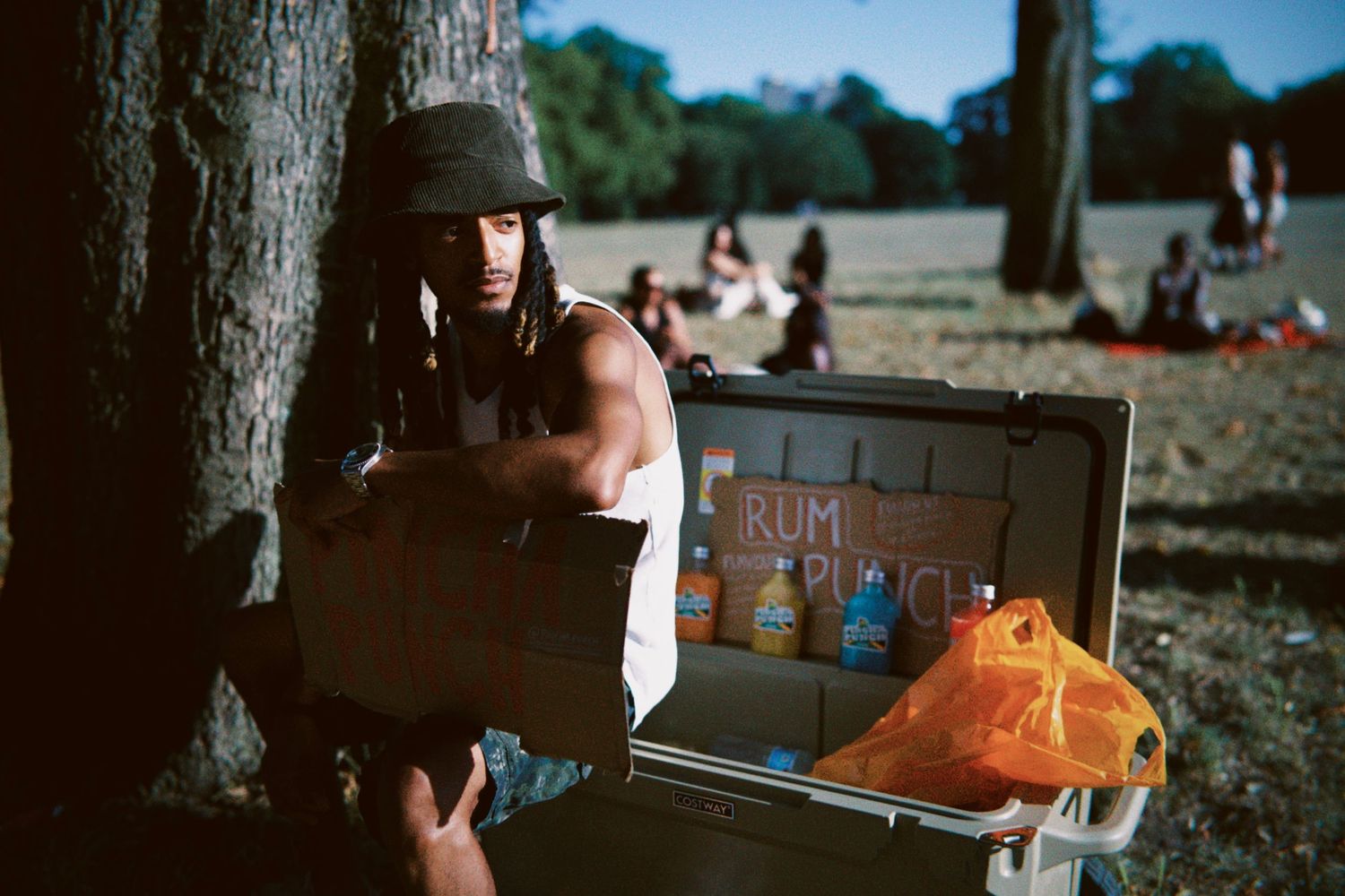 Man sitting next to a cooler stocked with Pincha Punch drinks at outdoor London event by ARIETA Studios.