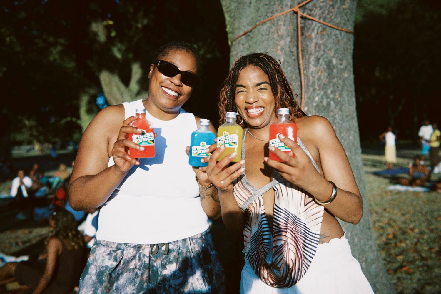 Two women holding colourful Pincha Punch tropical drinks at summer event by ARIETA Studios.