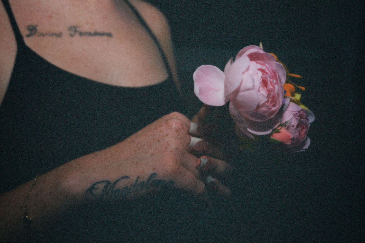 Close-up of hands holding white flowers, showing wrist tattoos and ring.