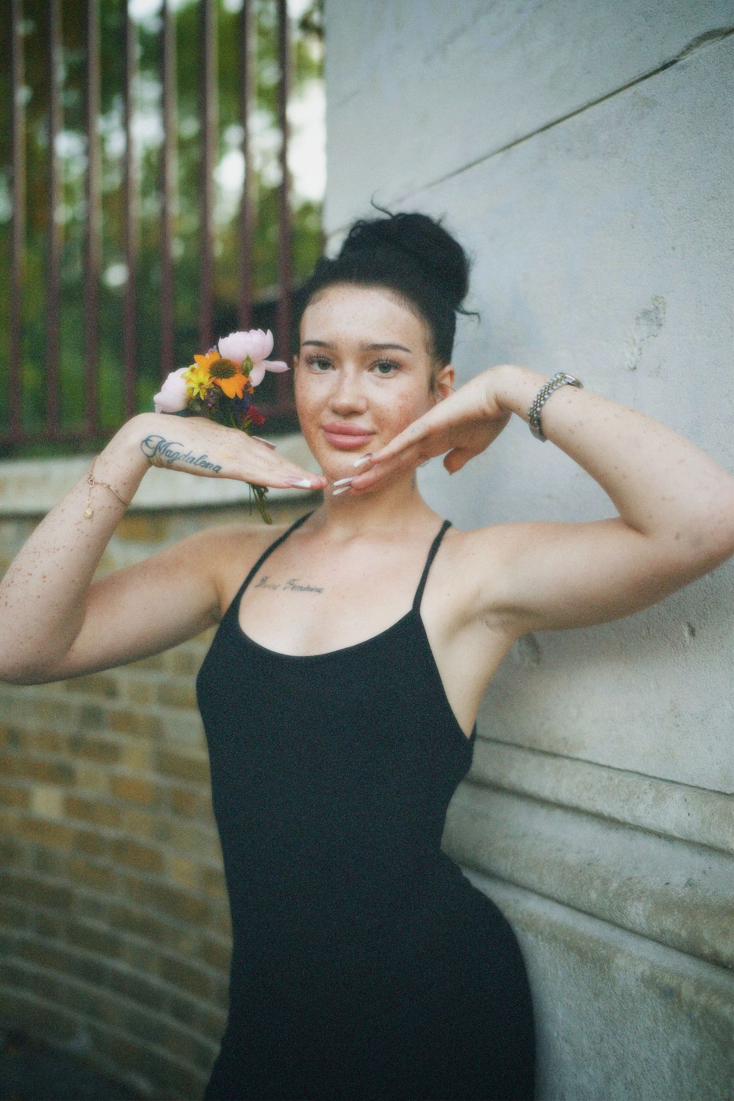Editorial portrait of a woman posing with flowers by her head in a black strap dress.