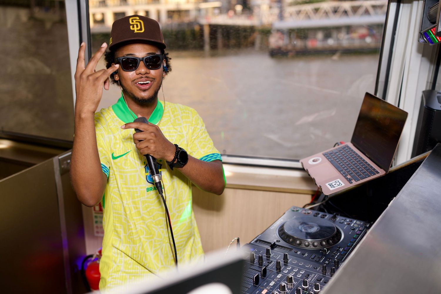DJ in a bright yellow shirt and sunglasses performing behind the decks.