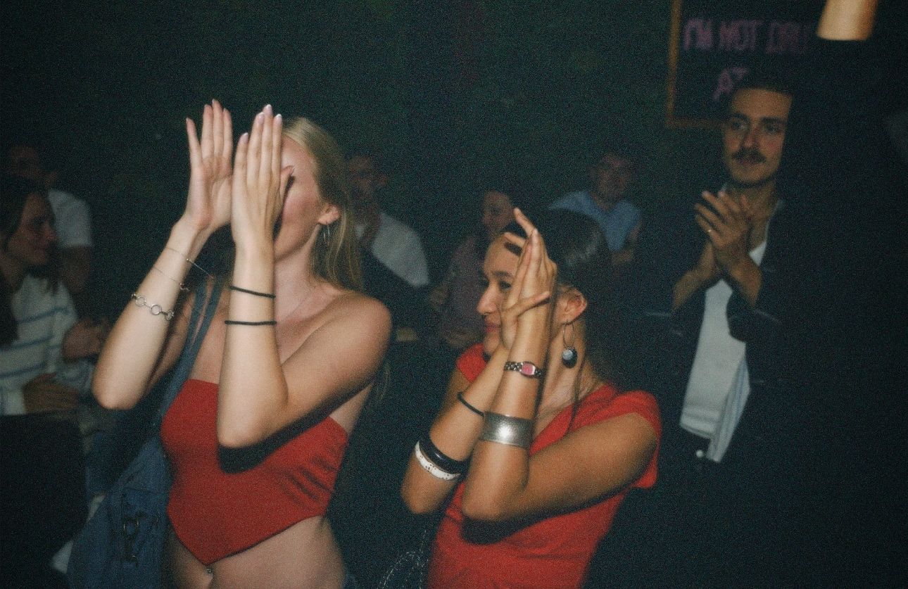 Two women in red tops gesturing and smiling during a live screening at a London pub covered by ARIETA Studios.