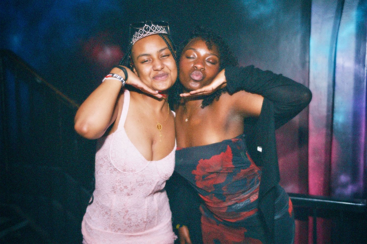 Two women smiling and posing together in colorful nightclub lighting.