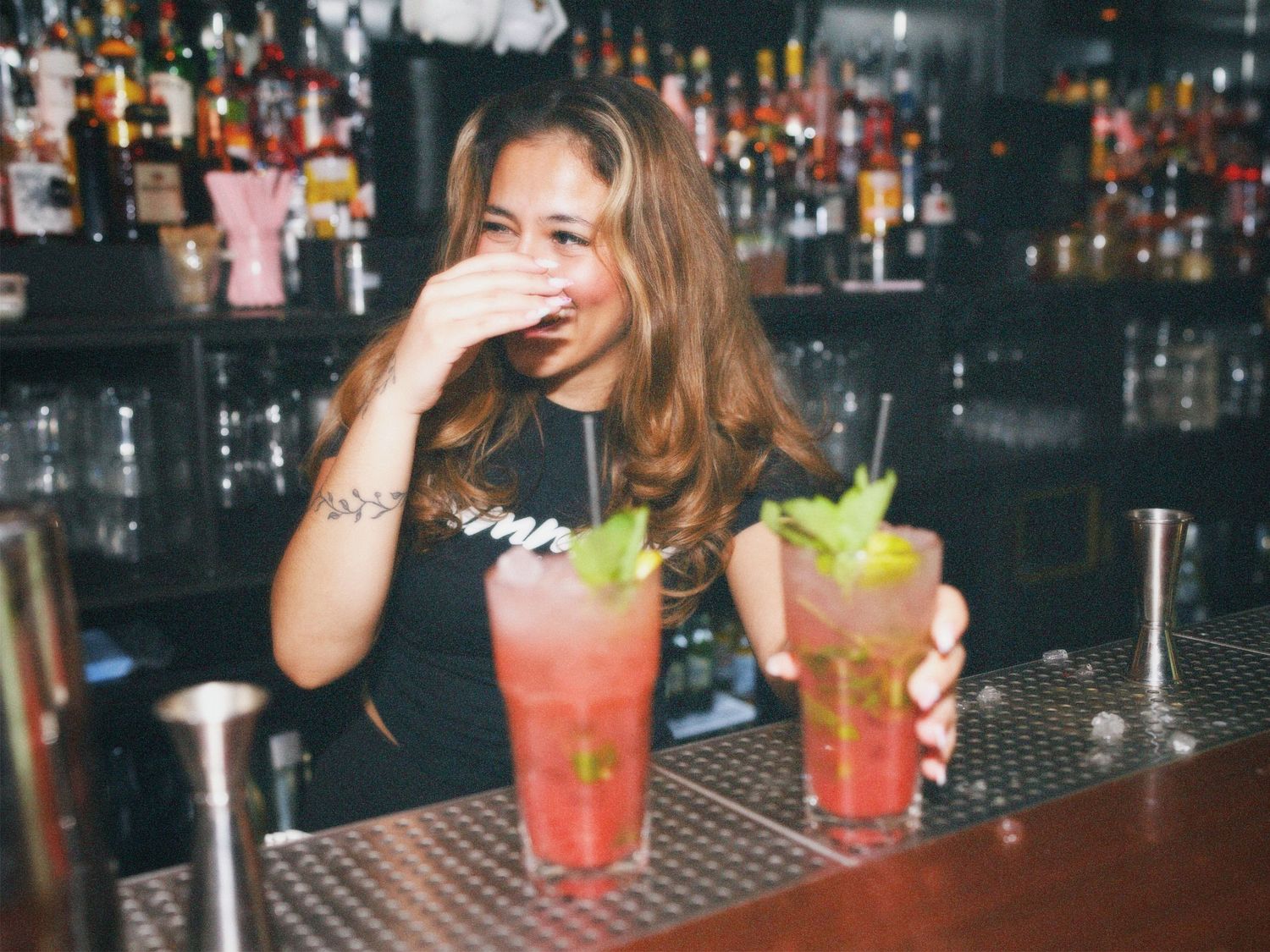 A laughing female bartender serving fresh mint cocktails at the Simmons Shoreditch bar counter. Photo by ARIETA Studios.