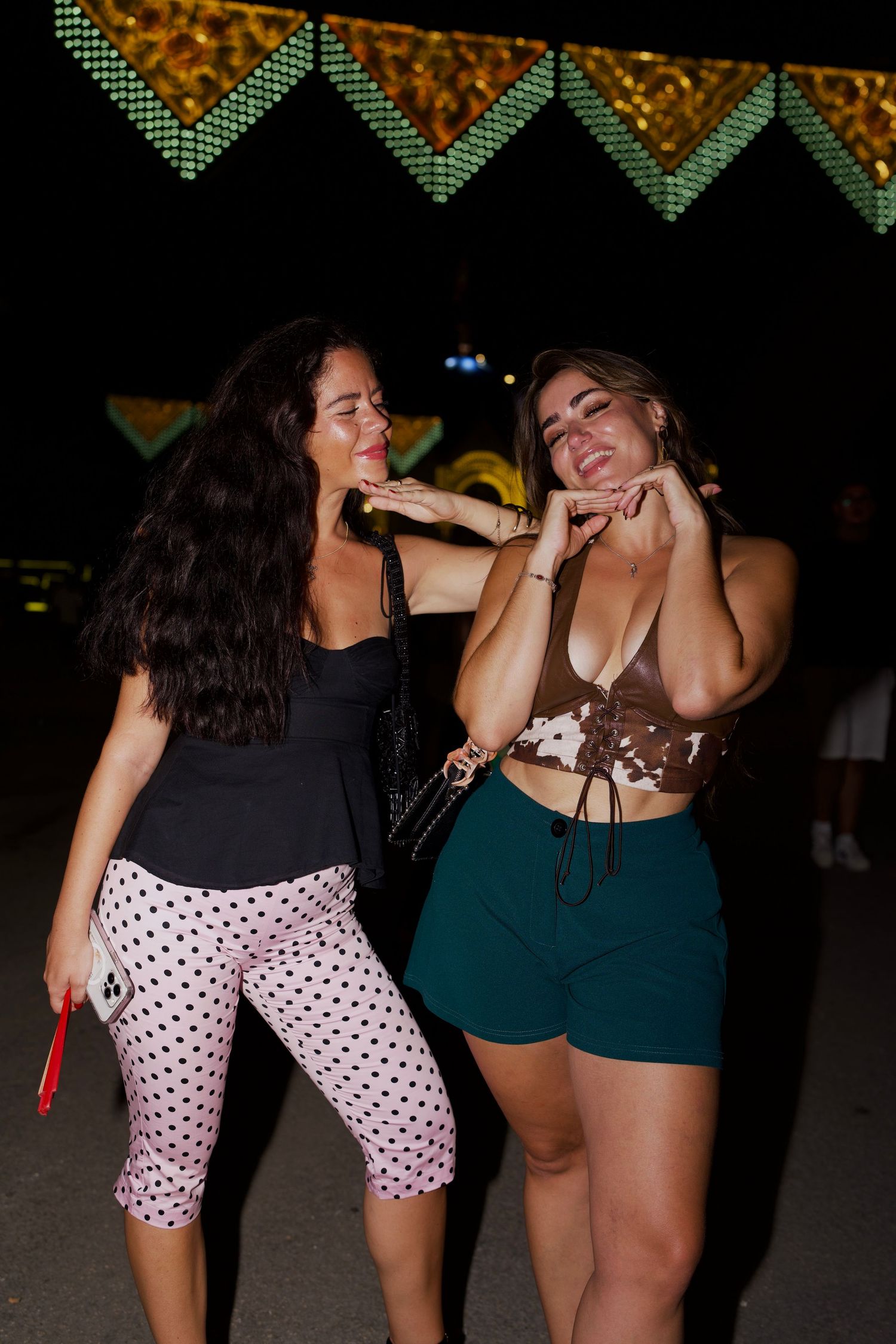 Two women posing under night lights / Dos mujeres posando bajo las luces de la Feria.