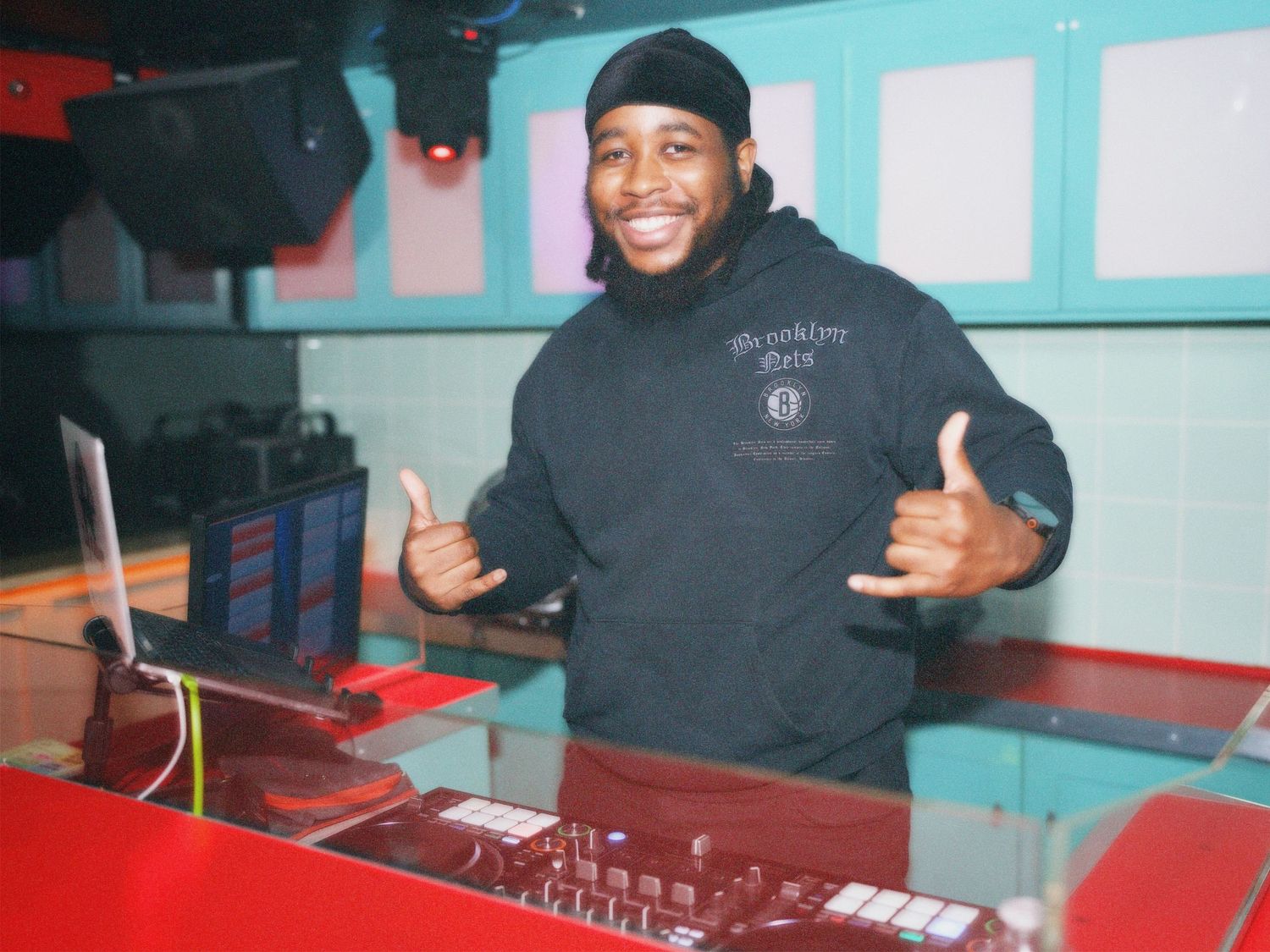 A smiling DJ giving a thumbs-up behind his mixing console at a vibrant London venue party. Captured by ARIETA Studios.