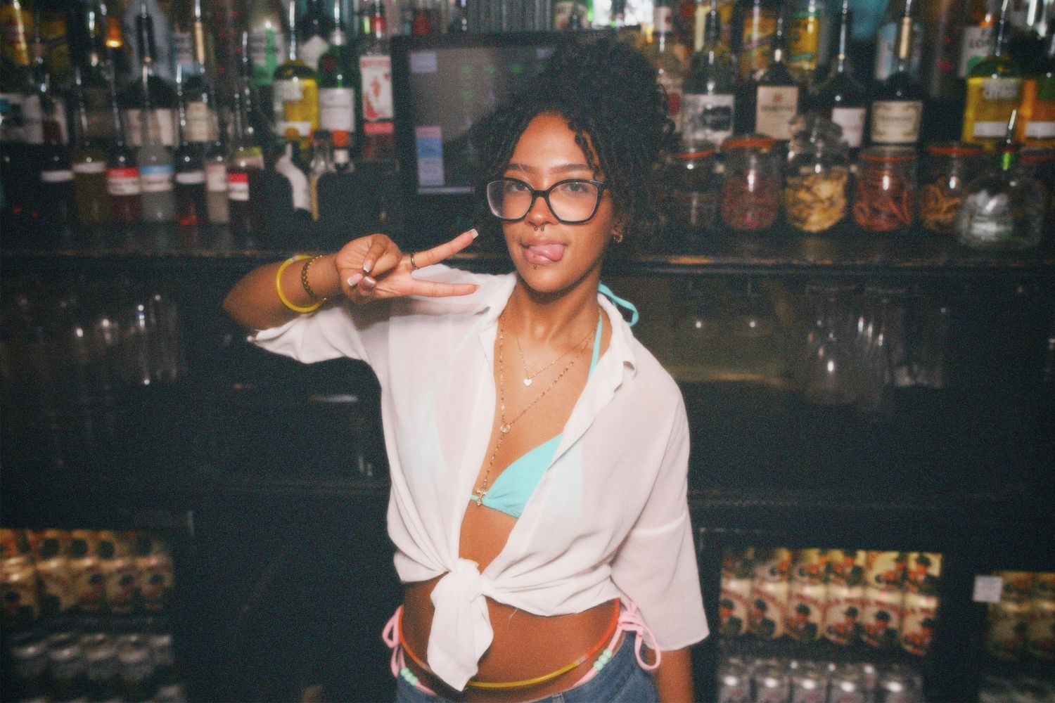 Woman in white shirt giving peace sign at bar event captured by ARIETA Studios.