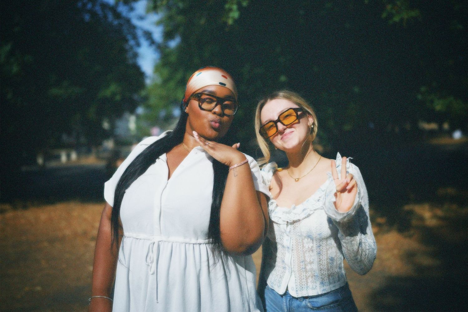Two friends smiling and standing shoulder to shoulder outdoors in summer light.
